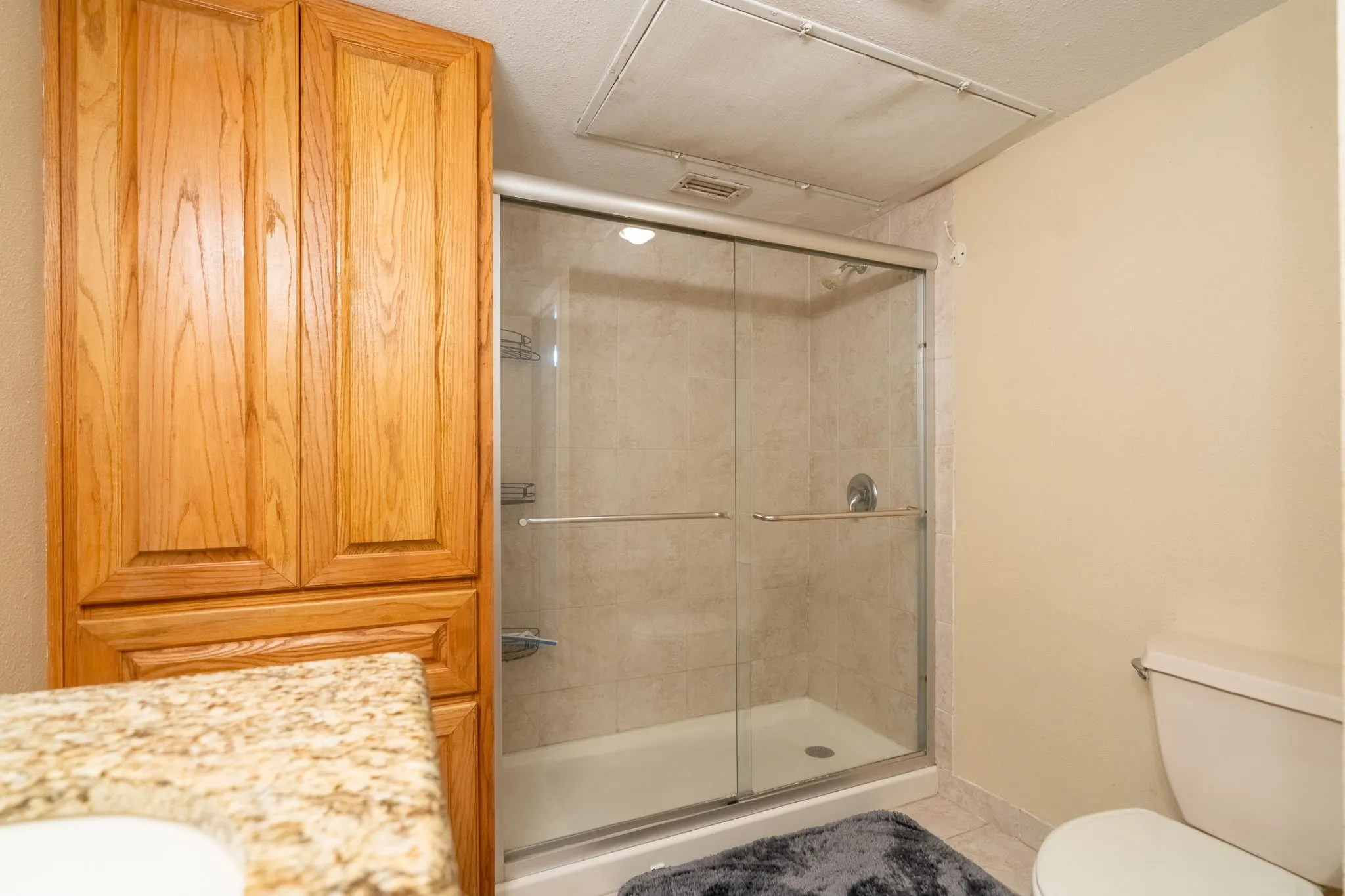Glass-enclosed shower with tile surround, wood-finish cabinetry, and a granite-patterned countertop