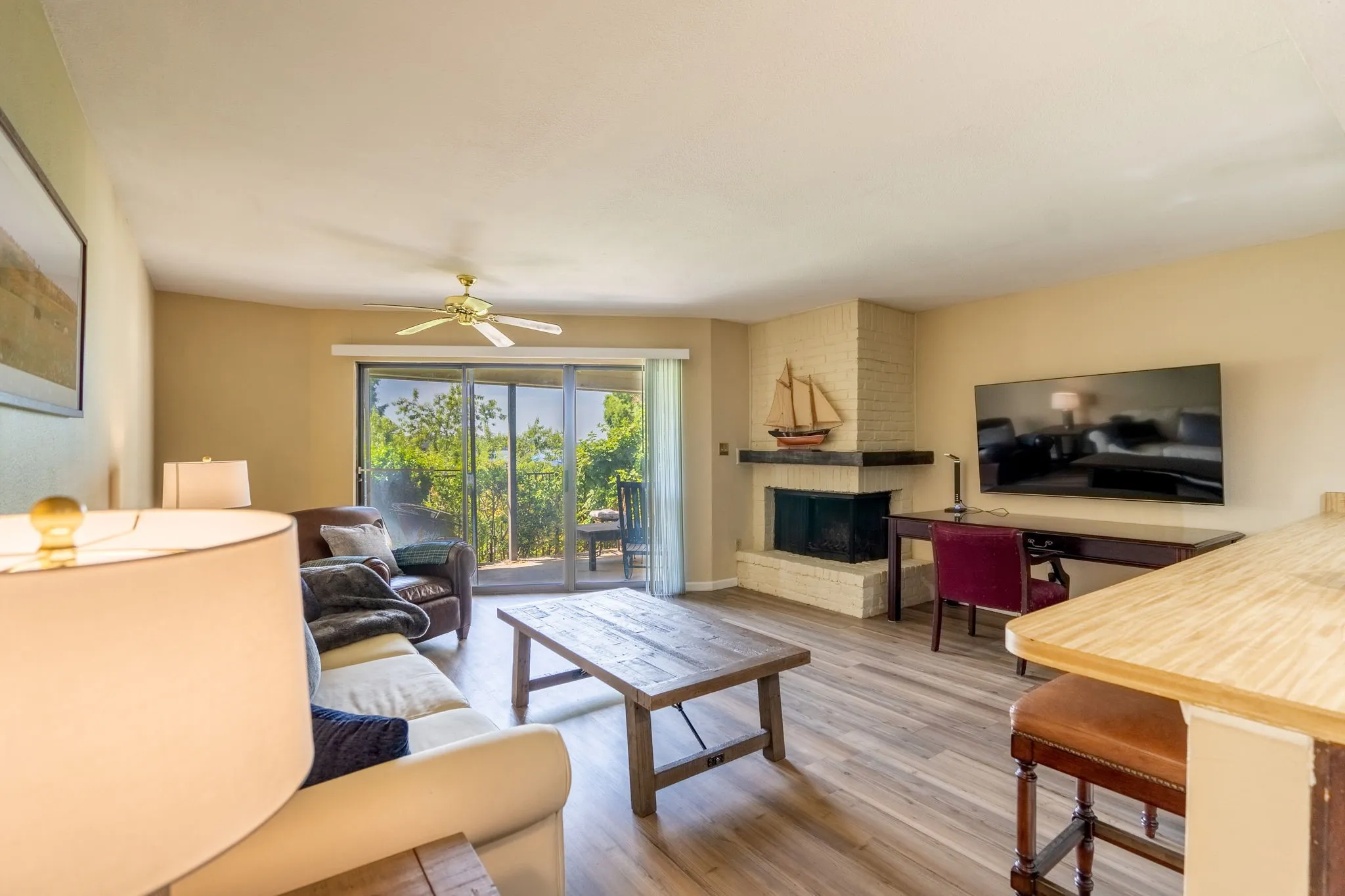Spacious living area featuring wood-finish flooring, a white brick fireplace, and sliding glass doors opening to an outdoor patio