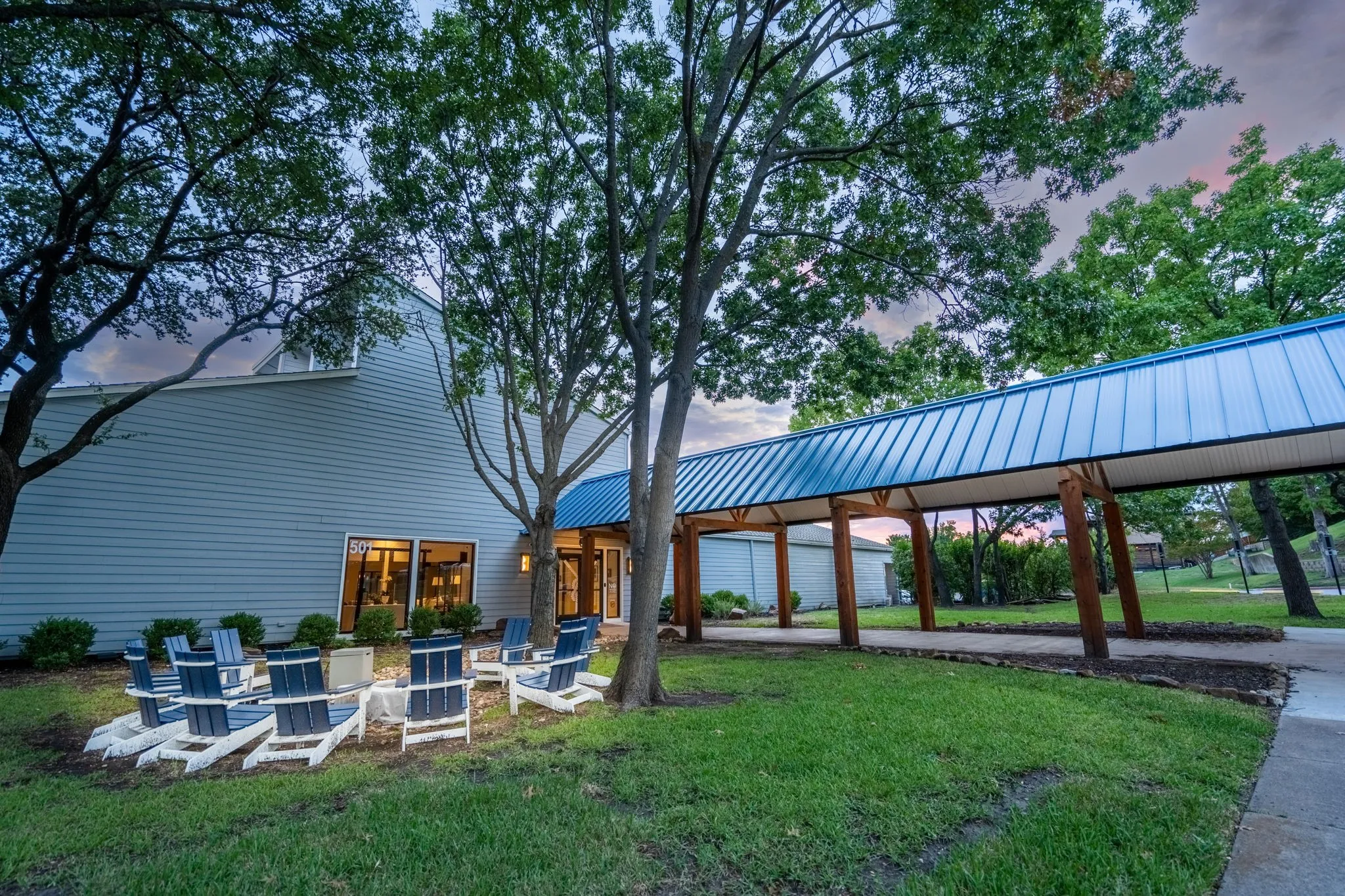 Exterior featuring light blue siding, a blue metal roof on an awning, and mature trees