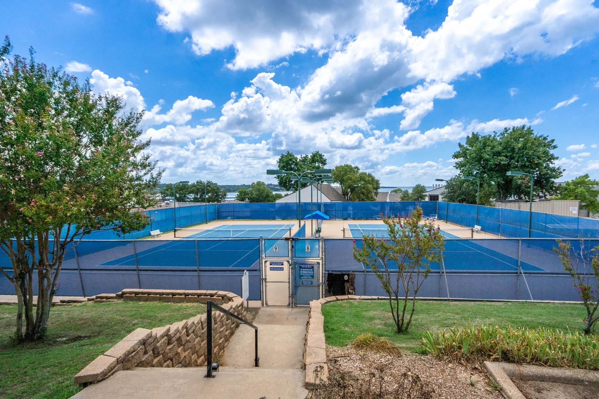 Multiple blue-surfaced tennis courts with perimeter fencing