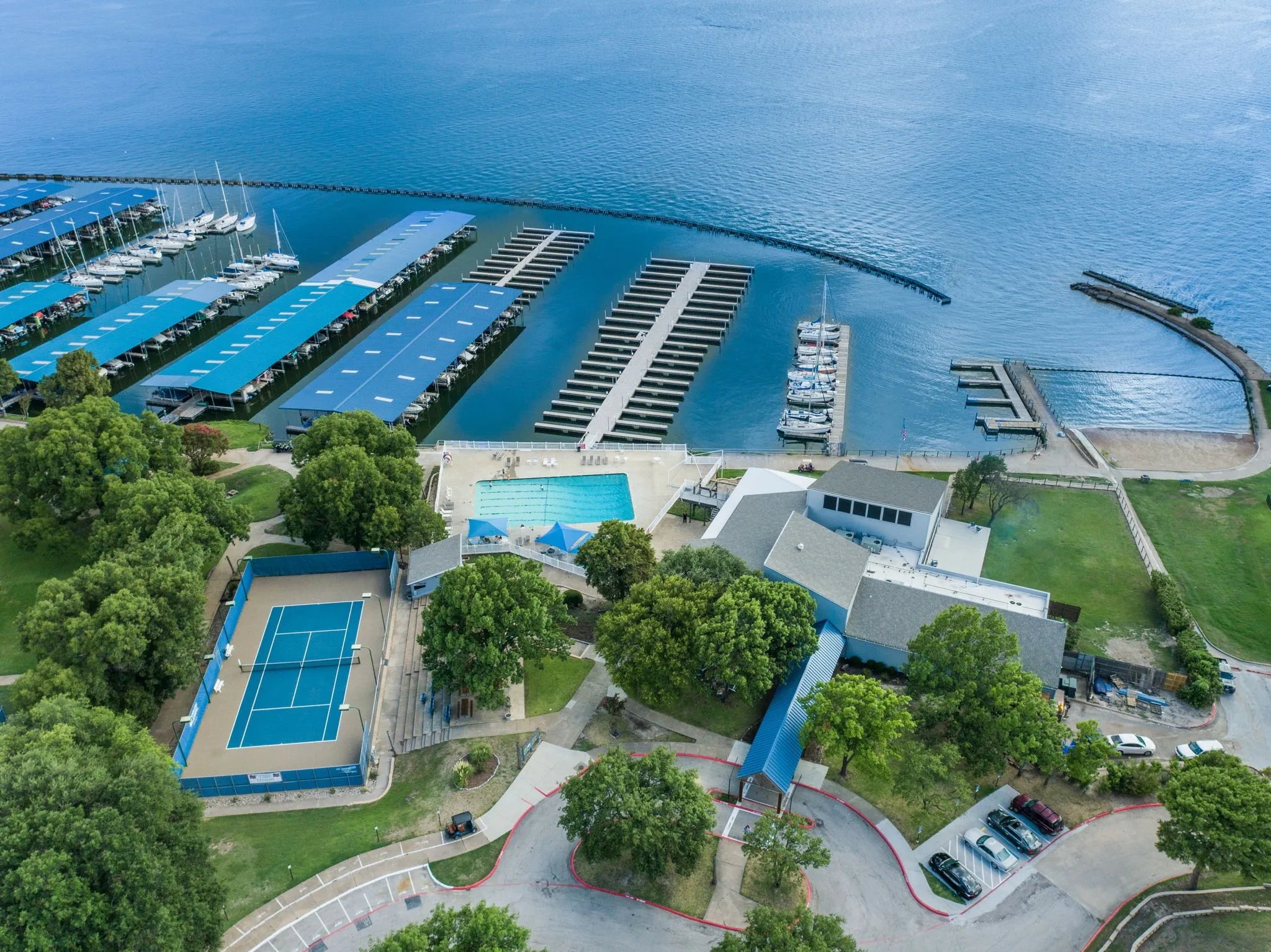 Waterfront property featuring extensive boat slips, a large swimming pool, a tennis court, and a multi-level building