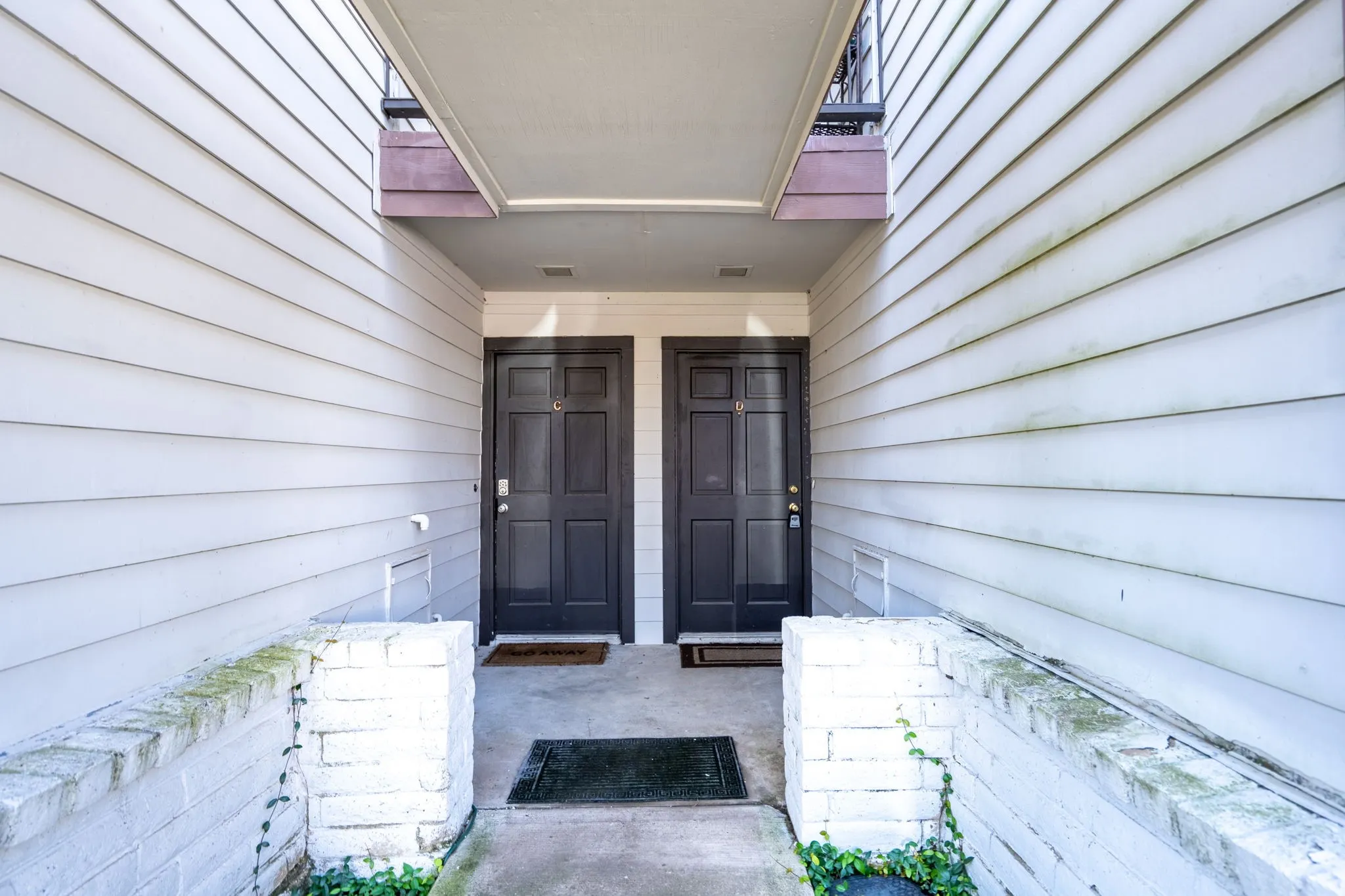 Siding exterior with two dark paneled entry doors, an overhead balcony, and a concrete pathway