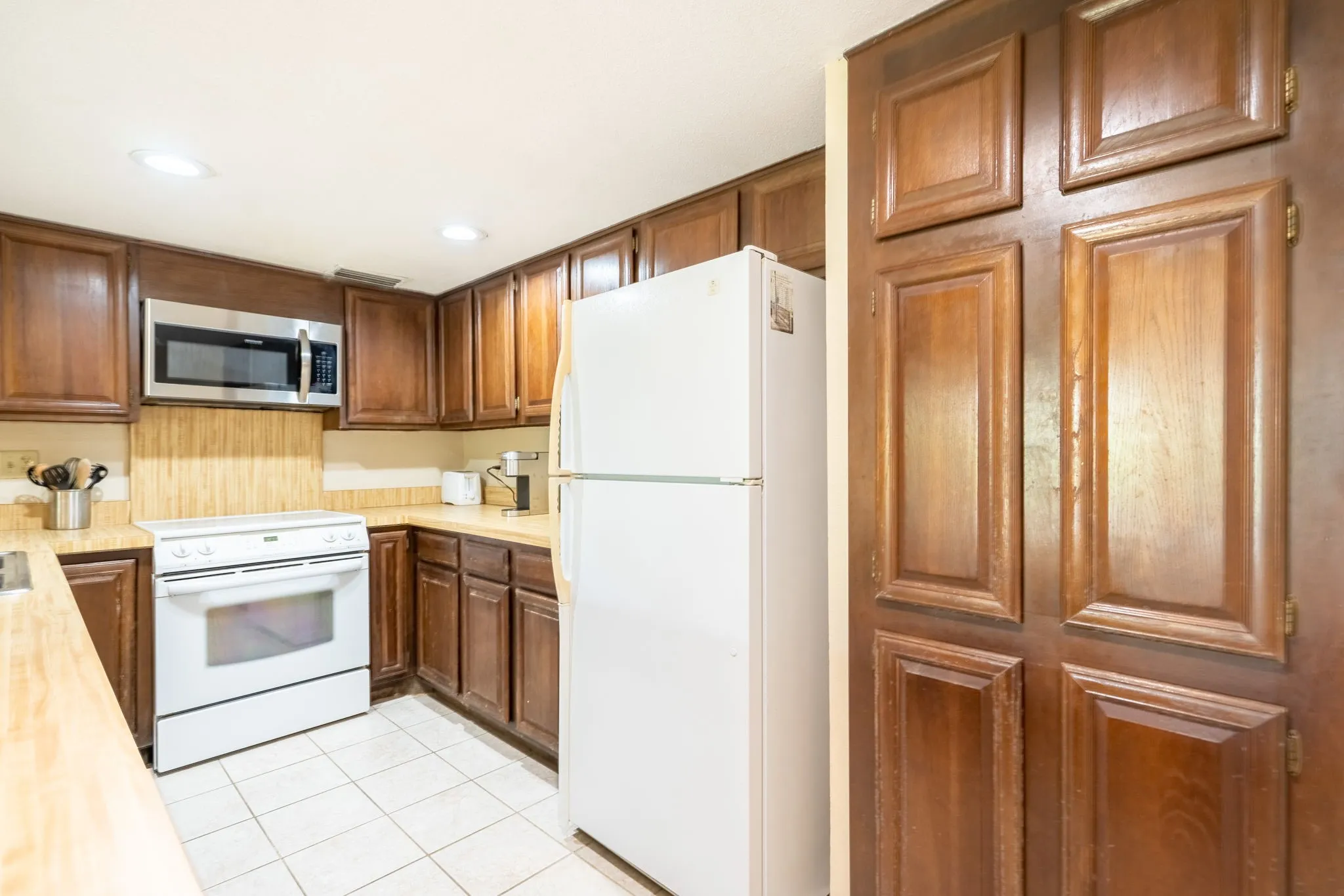 Wood-finish cabinetry, stainless steel microwave, white range, tile flooring, and recessed lighting