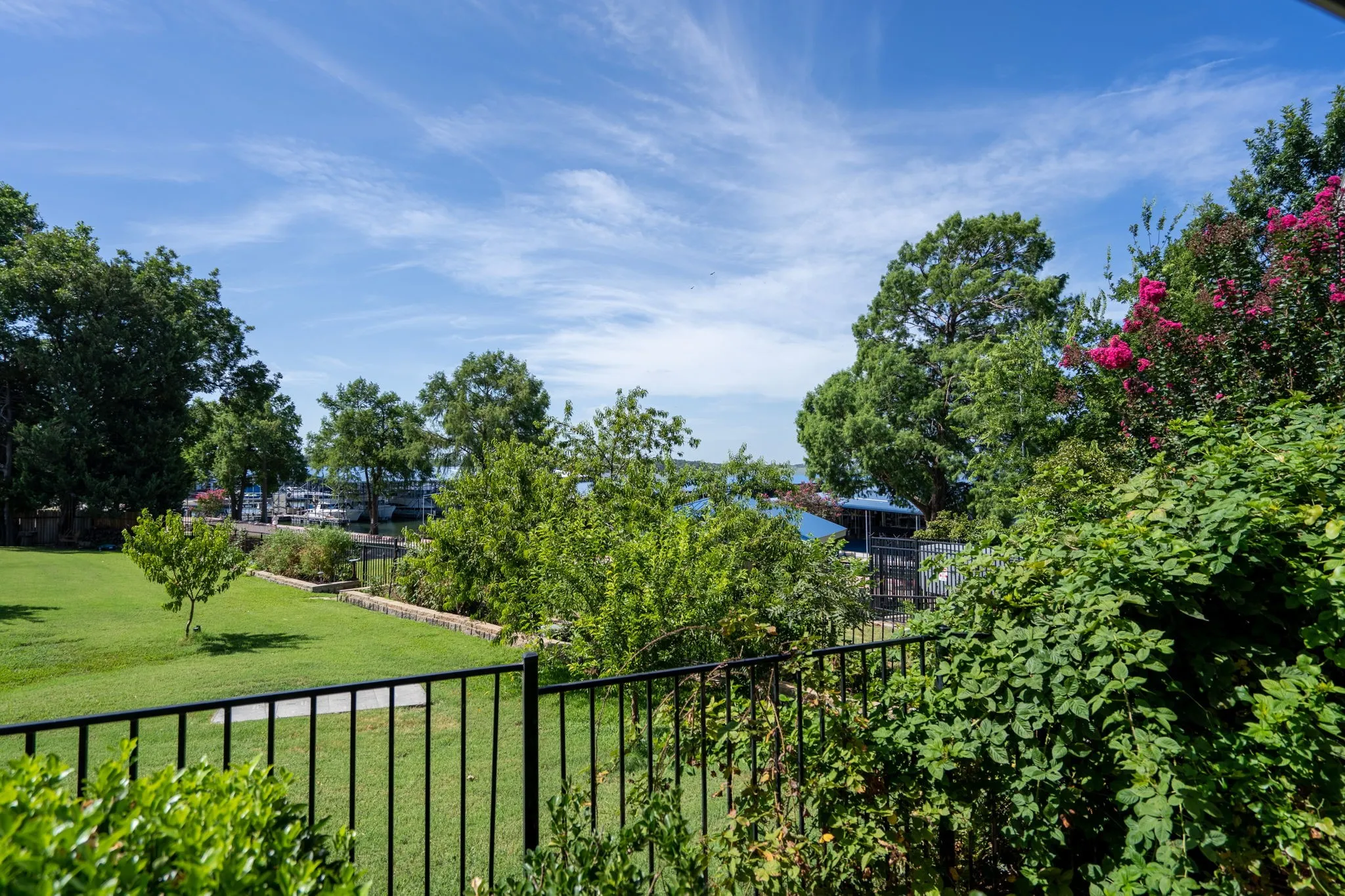Landscaped grounds with a black metal fence, mature trees, and flowering shrubs