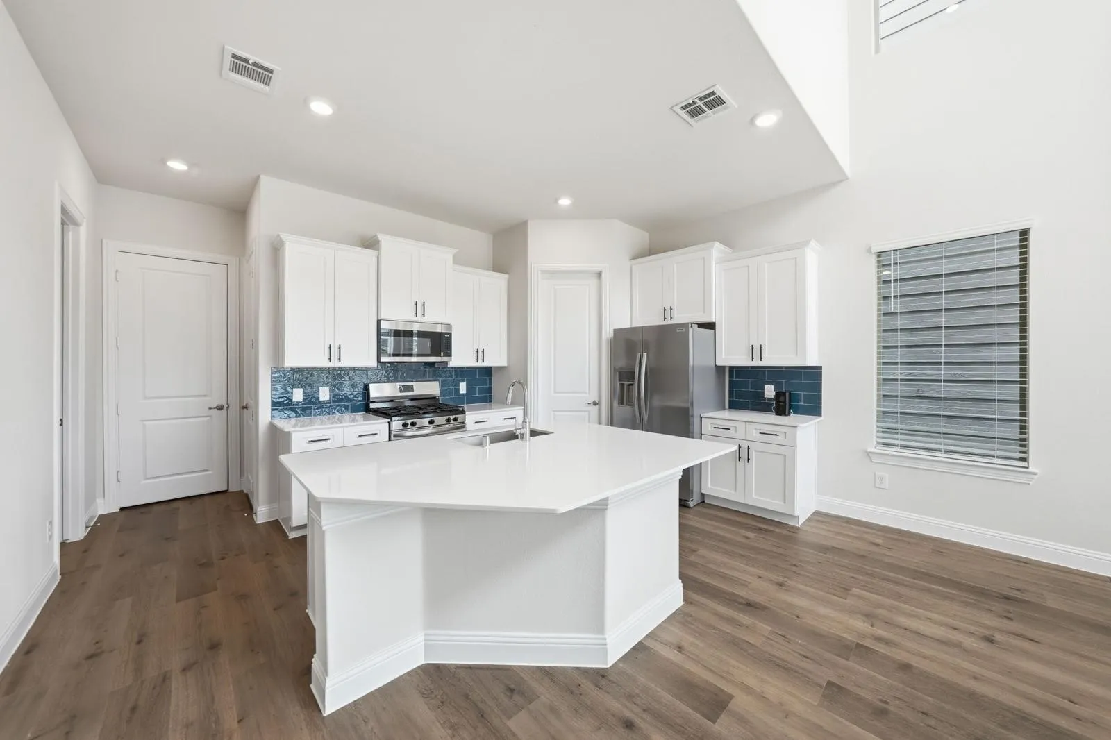 Kitchen featuring wood-finish flooring, white cabinetry with silver hardware, a stainless steel gas range, a stainless steel microwave, and a center island with a white countertop