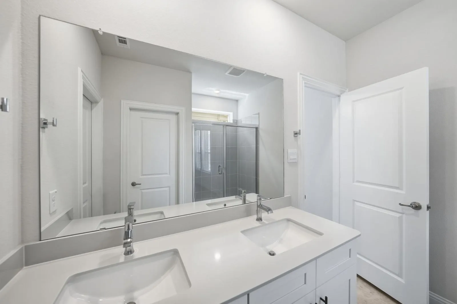 Dual undermount sinks with chrome faucets, expansive mirror, and a glass-enclosed shower