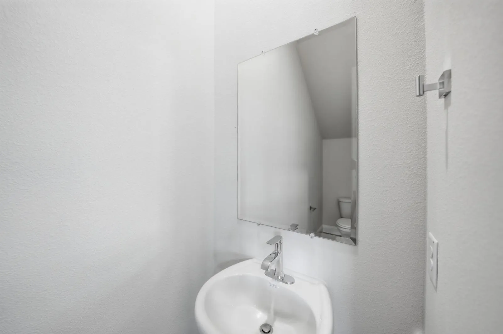 Wall-mounted mirror over a white porcelain pedestal sink with a chrome faucet
