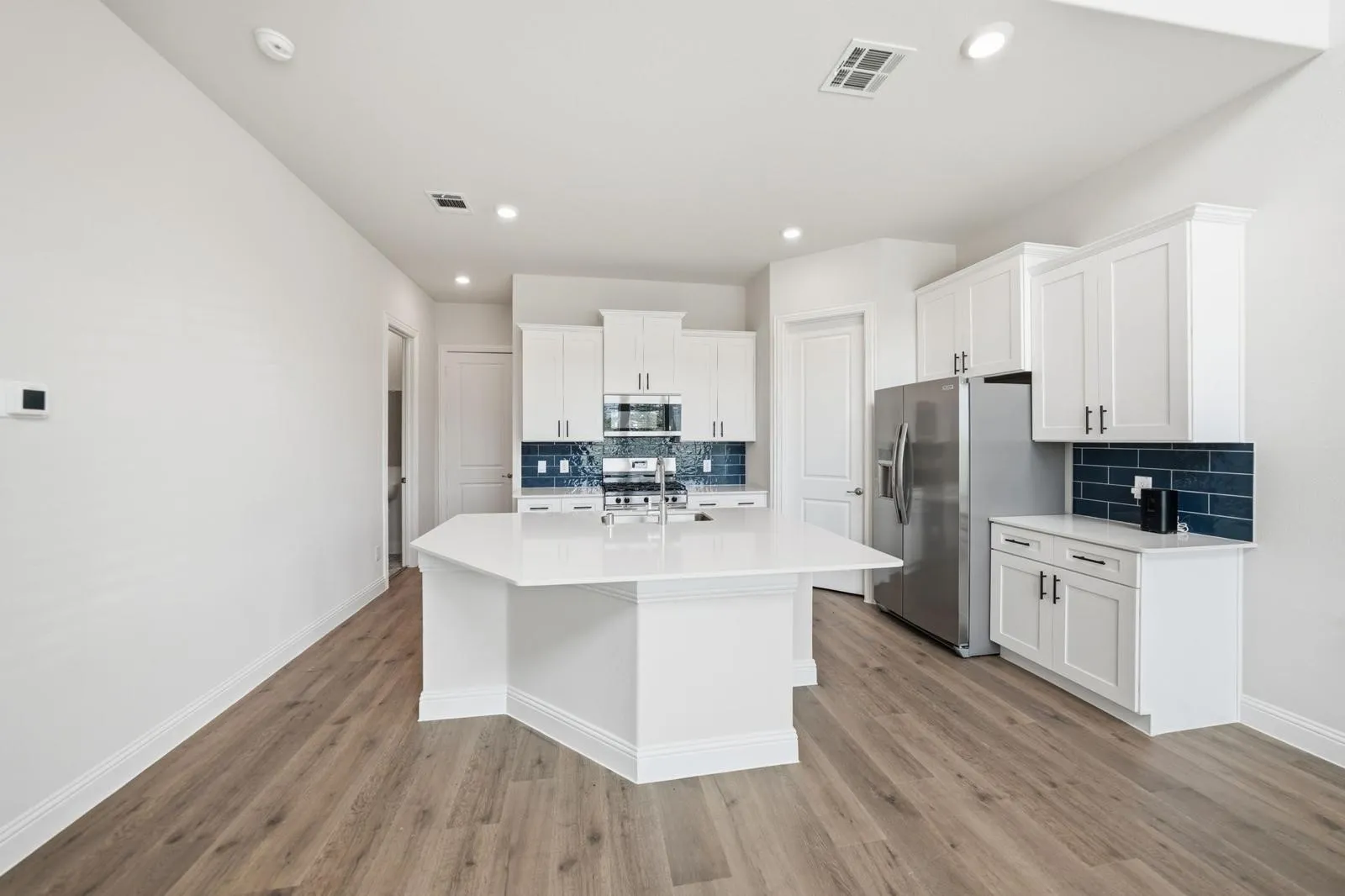 Modern kitchen featuring an angled island with a white countertop, white cabinetry with dark hardware, stainless steel appliances, and a blue subway tile backsplash