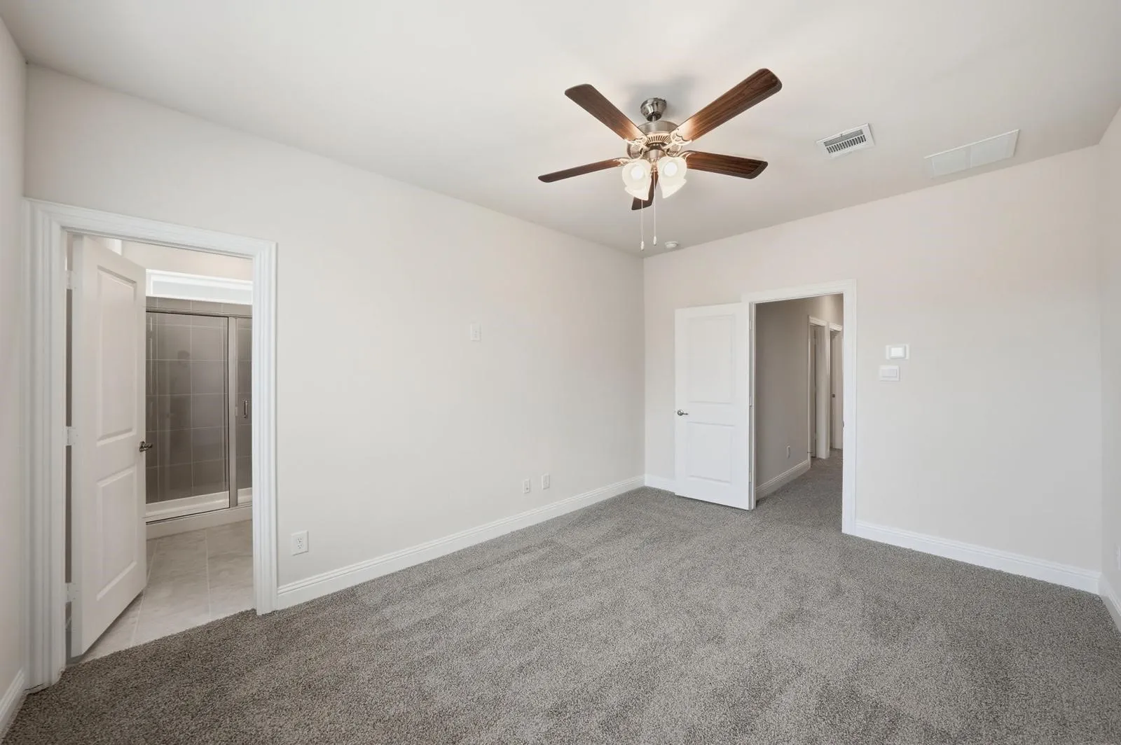 Gray carpet flooring, light neutral wall paint, wood-finish ceiling fan with integrated lighting, white interior doors, and a partial view of a bathroom with a glass-enclosed shower