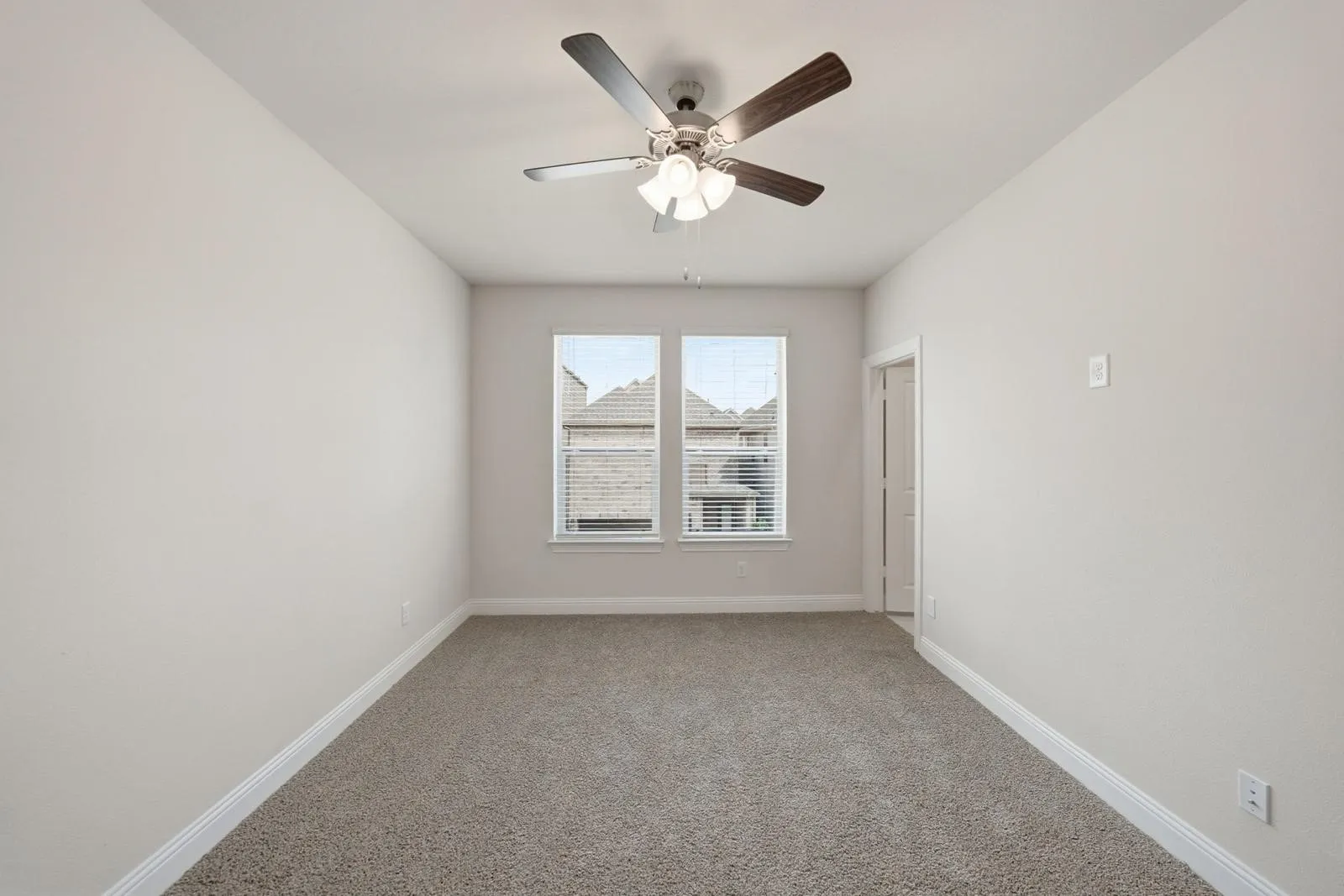 Room featuring neutral-toned carpeting, dual windows with blinds, a ceiling fan with integrated lighting, and a white interior door
