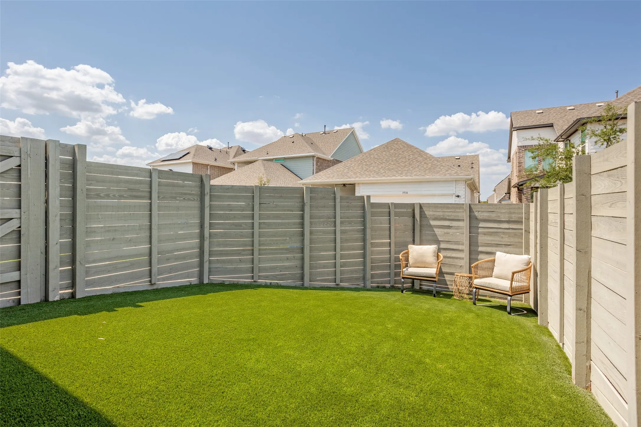 Enclosed backyard featuring a privacy fence, artificial turf, and a gated entry