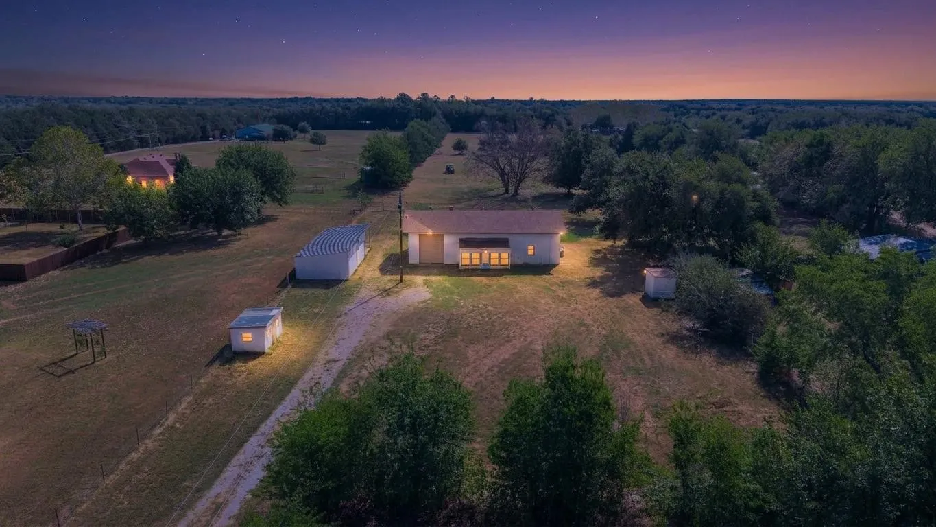 Single-story residence with a covered porch, surrounded by mature trees and open land