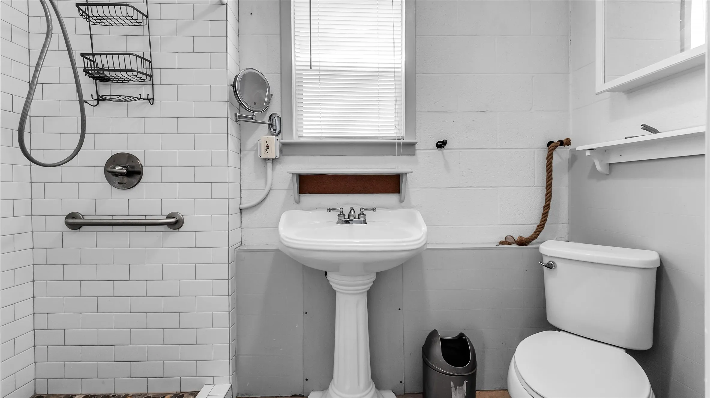 White subway tile shower with a stainless steel grab bar, a pedestal sink, and a toilet