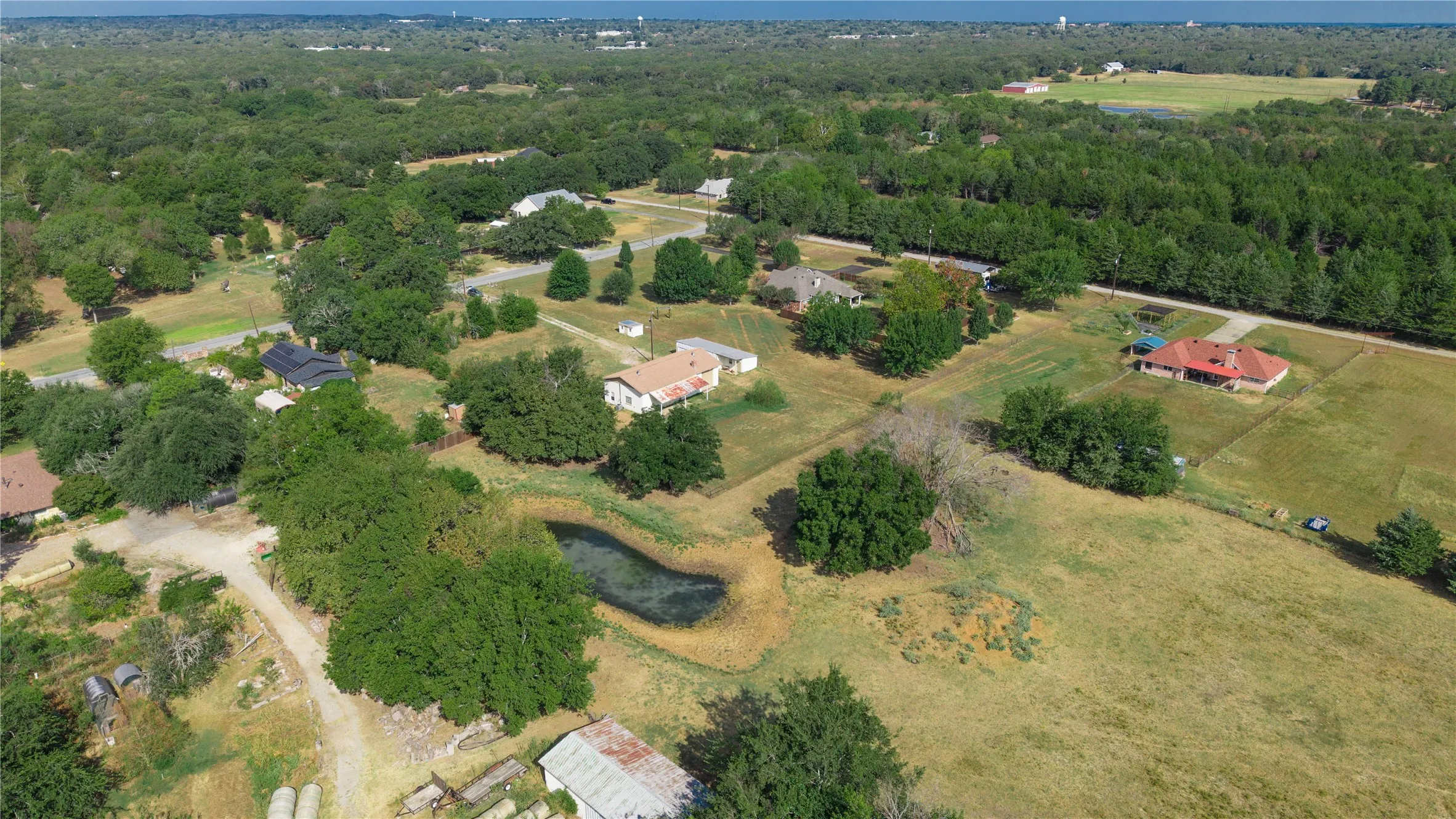Expansive rural landscape featuring wooded areas, open fields, and a visible pond
