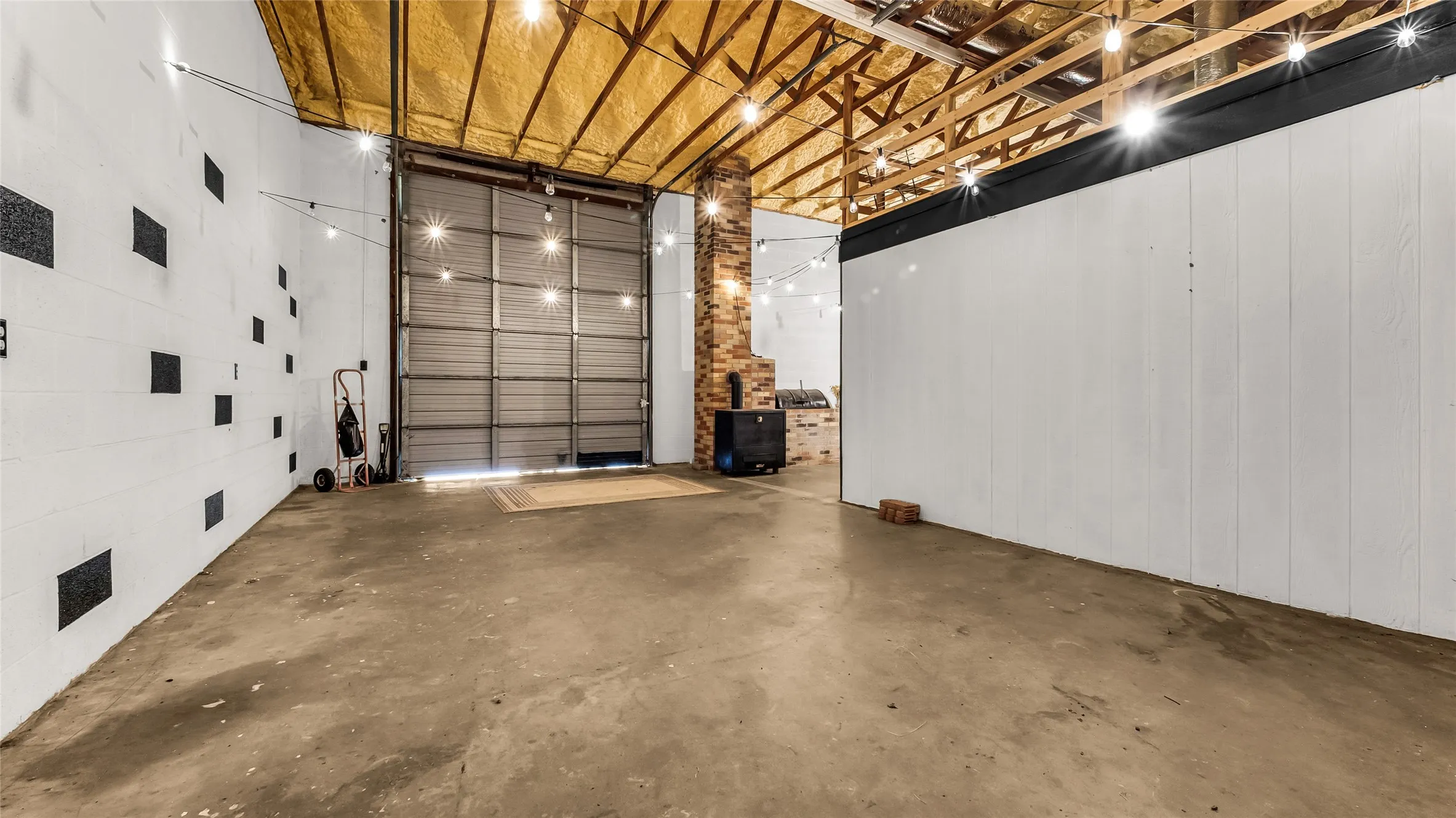 Exposed wood beam ceiling, concrete flooring, brick column, white paneling, and a large roll-up door