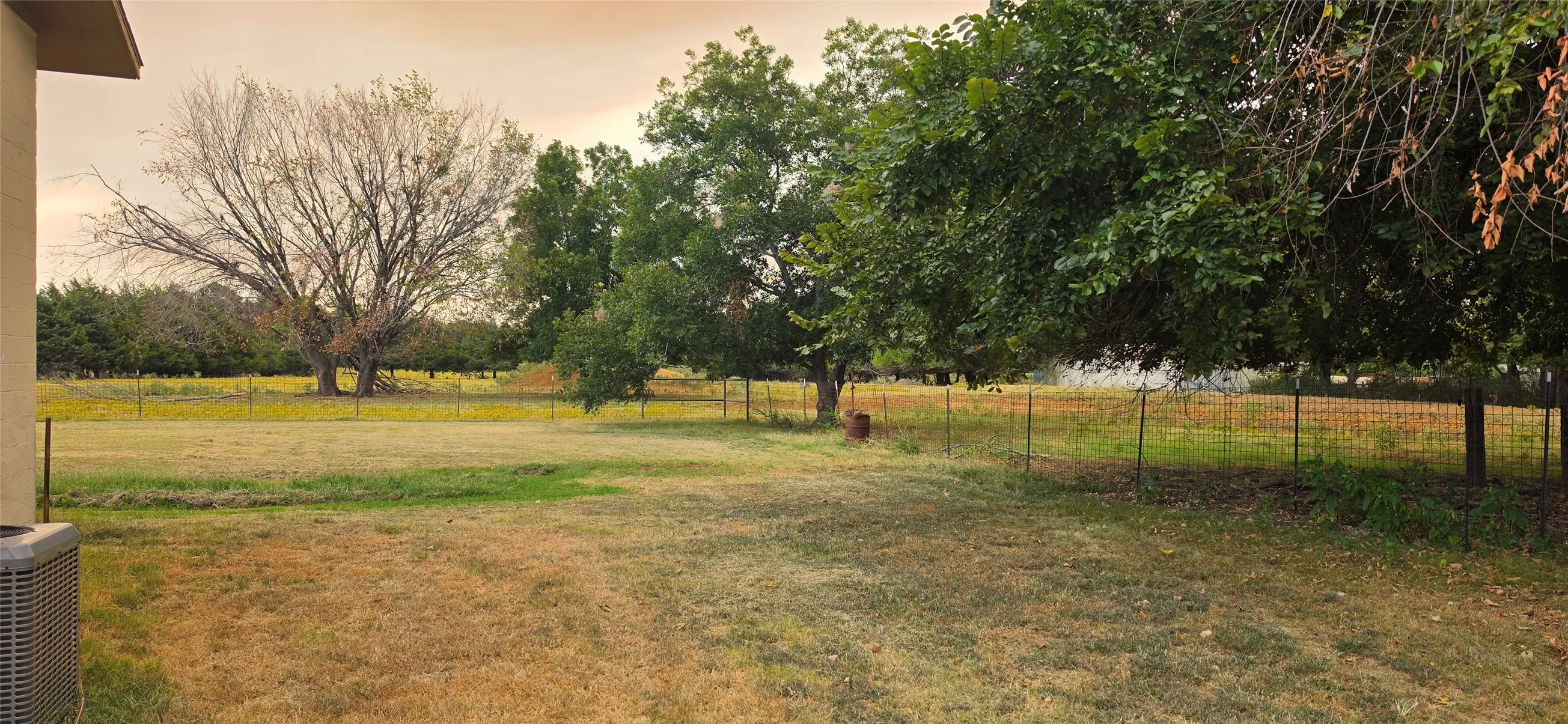Expansive exterior grounds featuring mature trees and a wire fence