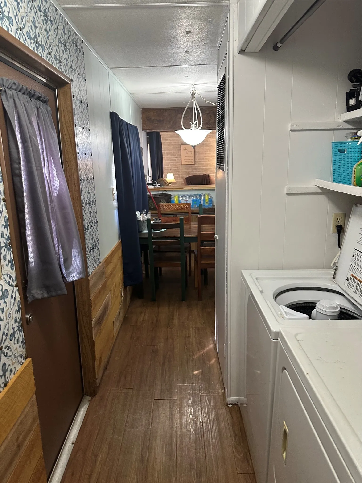 Wood-finish flooring throughout, white paneled walls, and a built-in laundry area with a washer