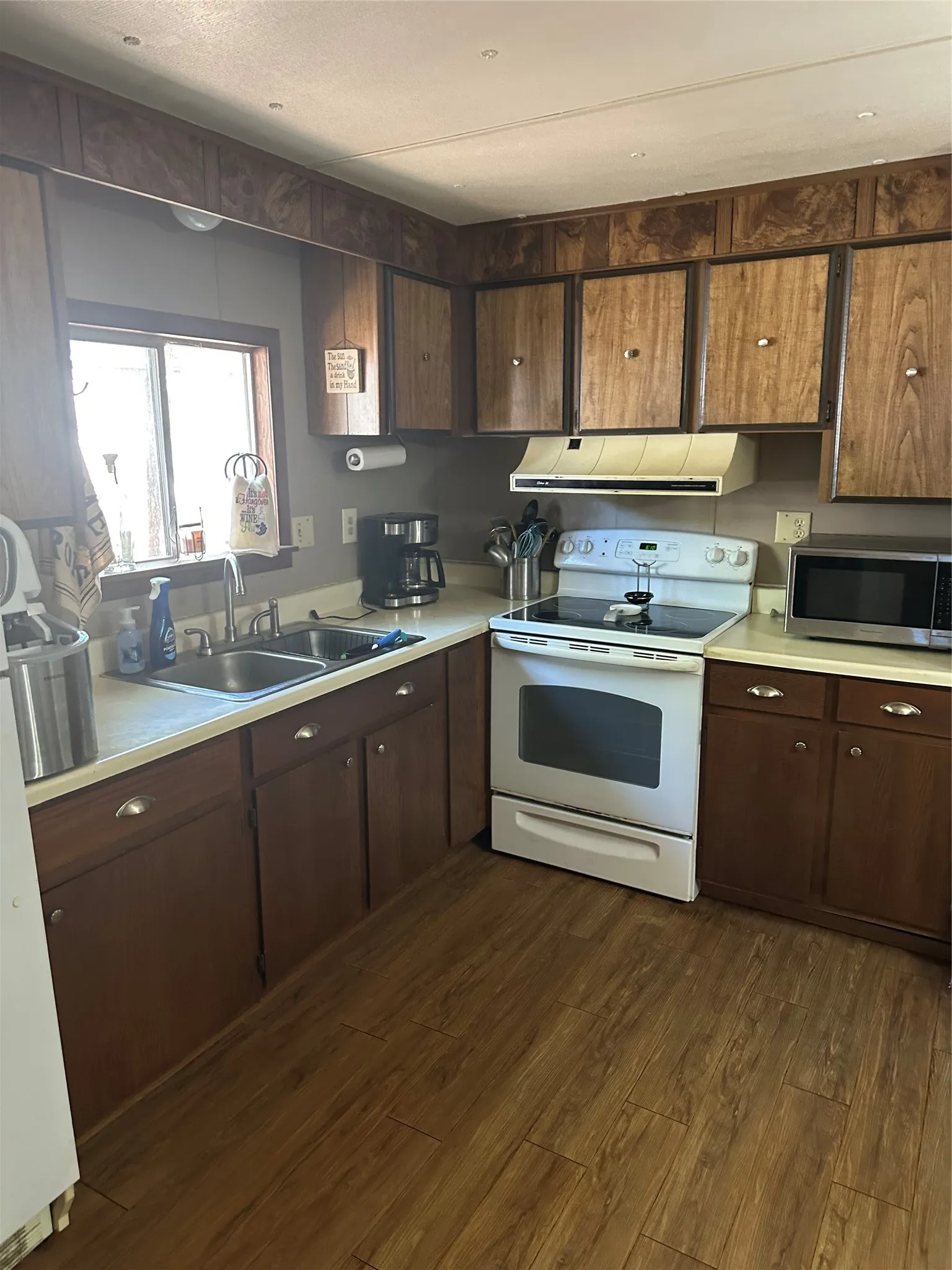 Kitchen featuring wood-finish flooring, wood-toned cabinetry, light-toned countertops, a dual basin stainless steel sink, and a window for natural light