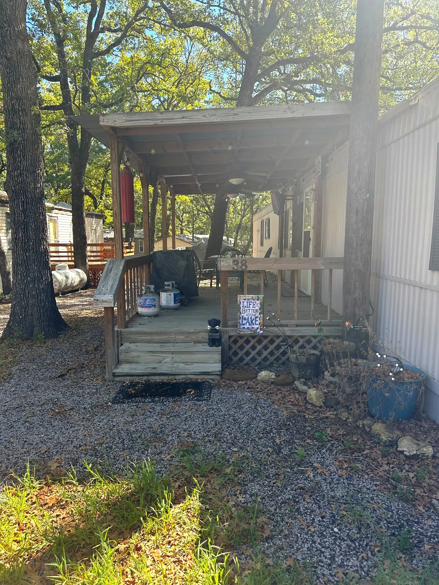 Covered porch with wood railing and steps, surrounded by mature trees