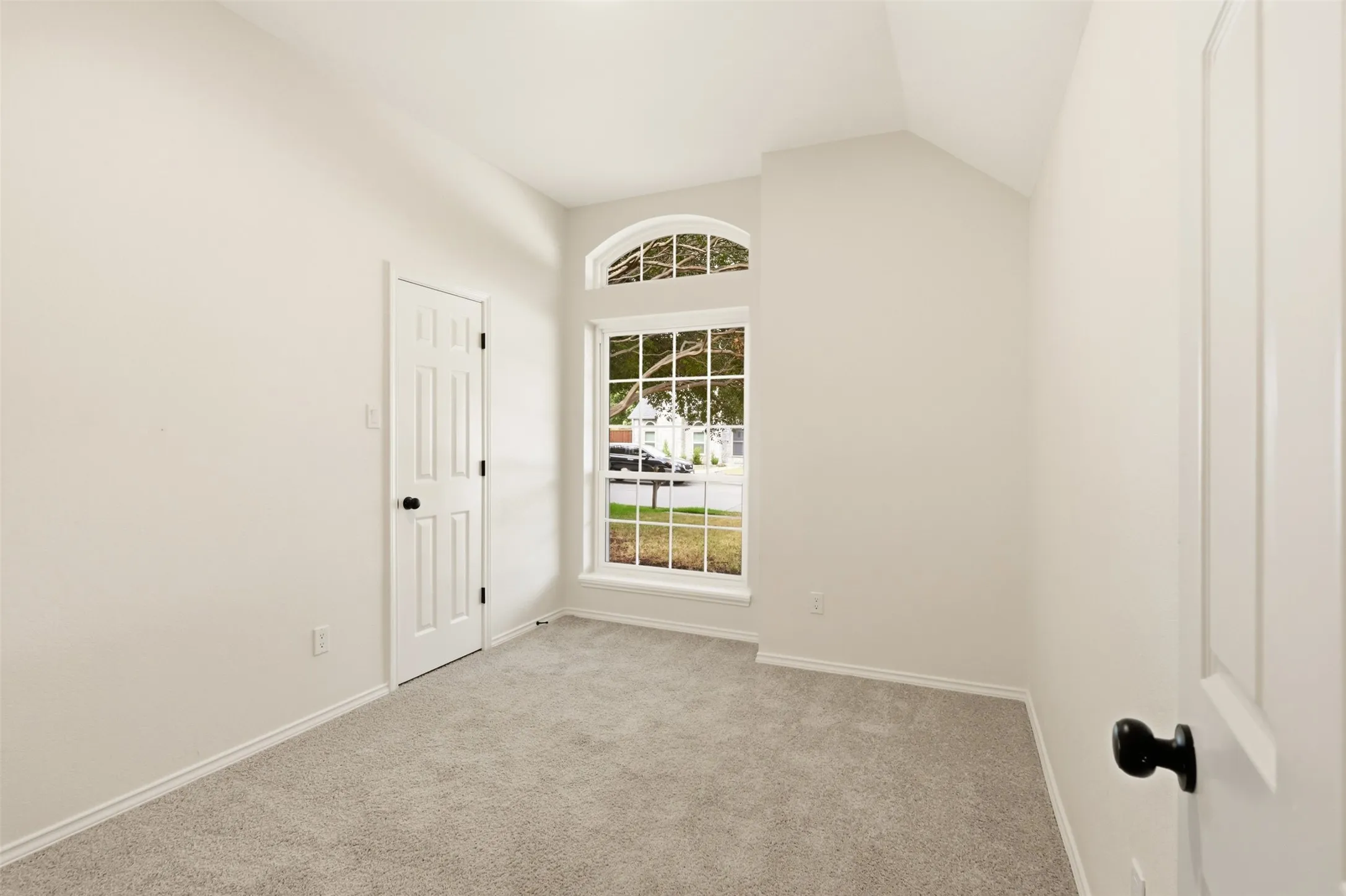 Room featuring vaulted ceiling, arched transom window, paneled doors, and gray carpeting