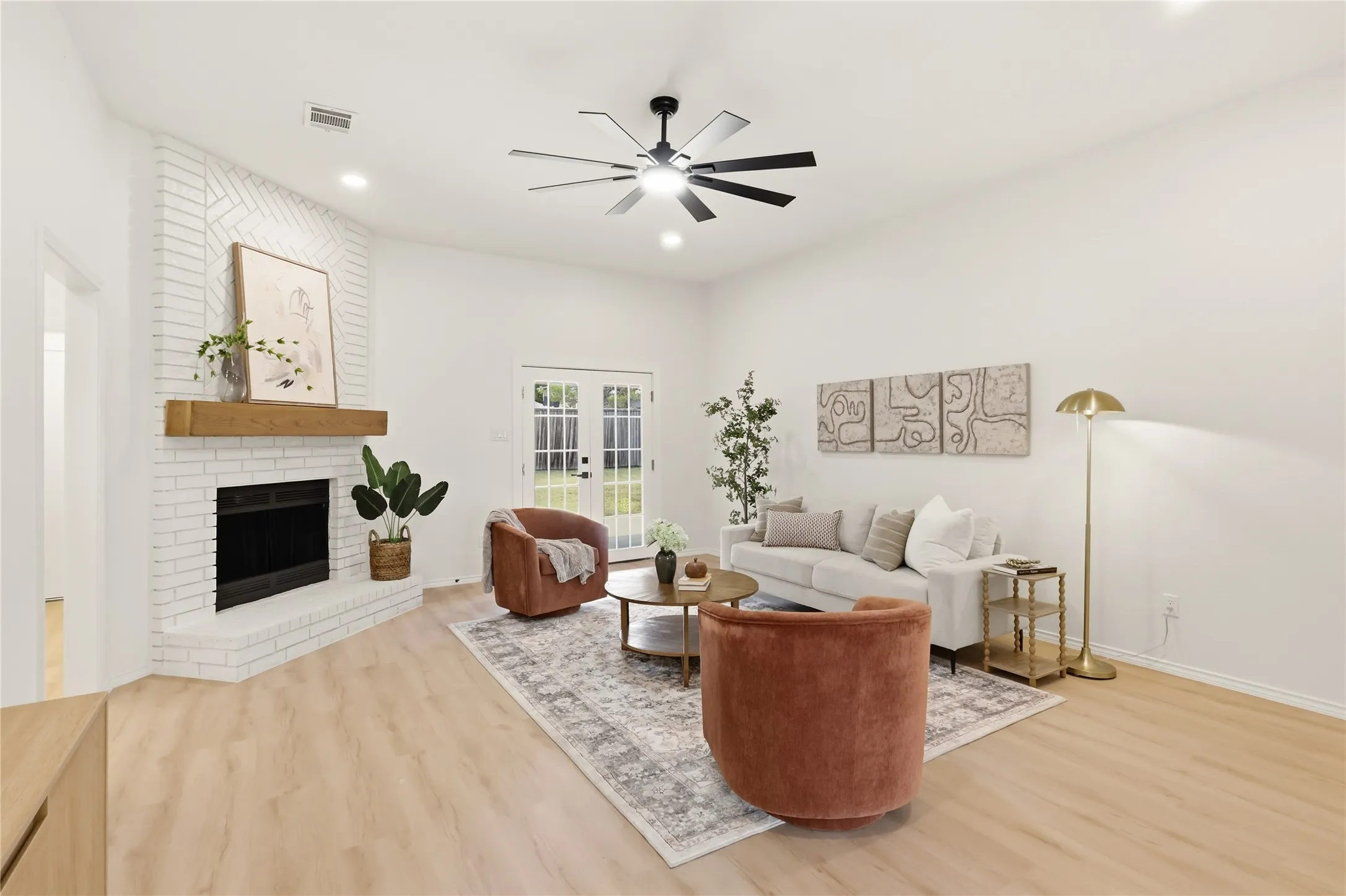 Bright living area with a white brick fireplace, wood mantel, and light wood-finish flooring