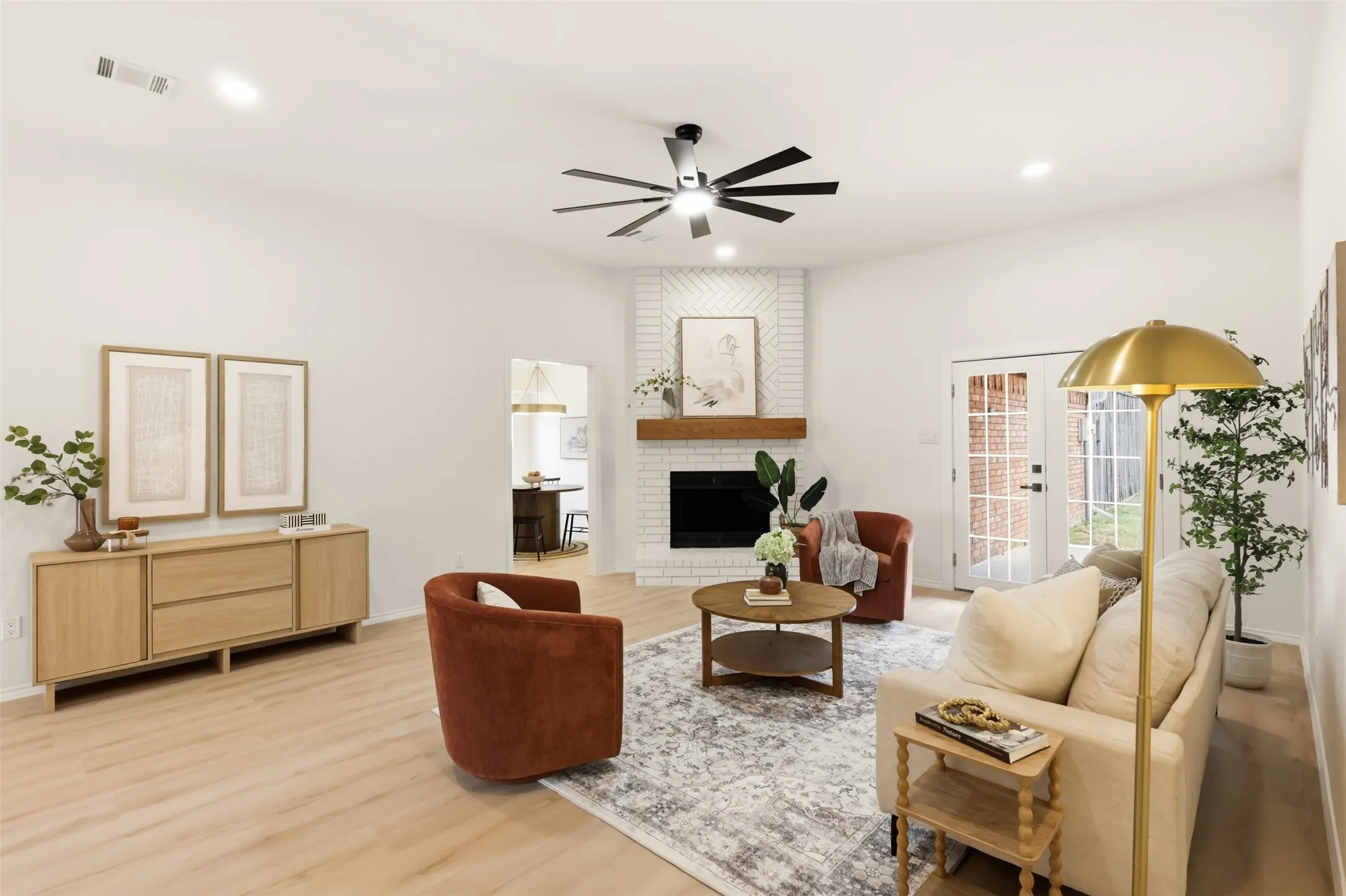 Wood-finish flooring, white brick fireplace with wood mantel, ceiling fan, recessed lighting, and double glass-paned doors