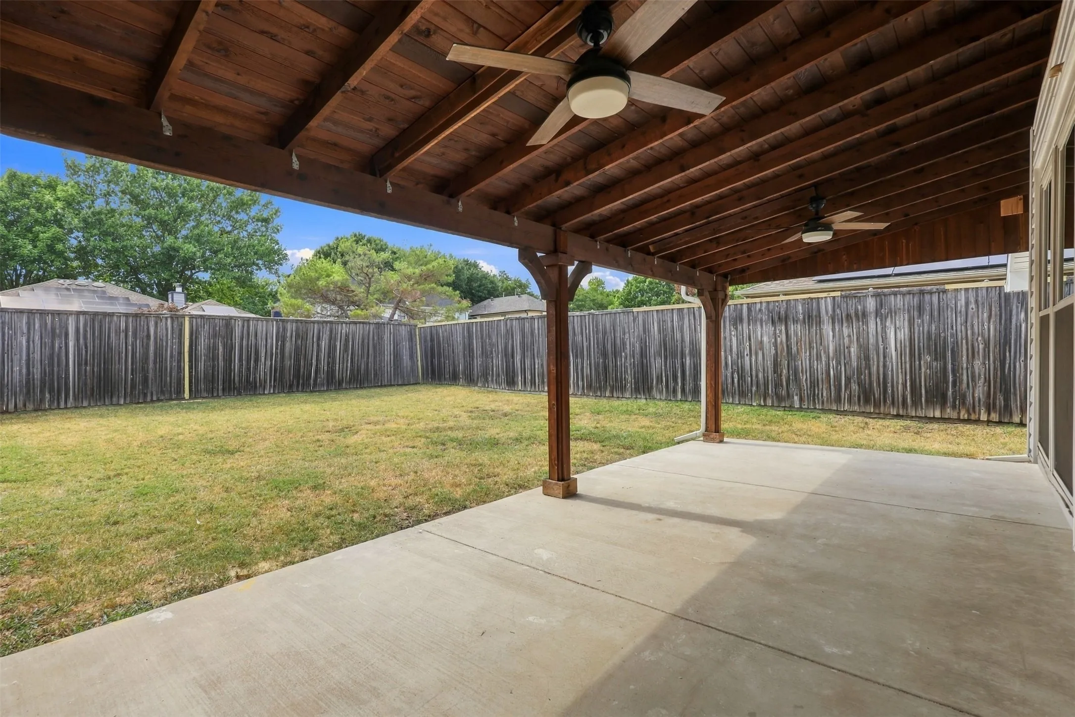 Expansive concrete patio with a wood-beamed ceiling and integrated ceiling fans