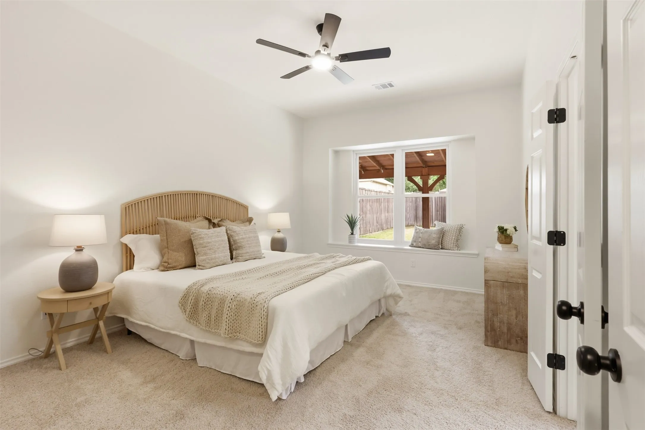 Recessed window alcove, ceiling fan, white paneled door, black door hardware, and light-toned carpet