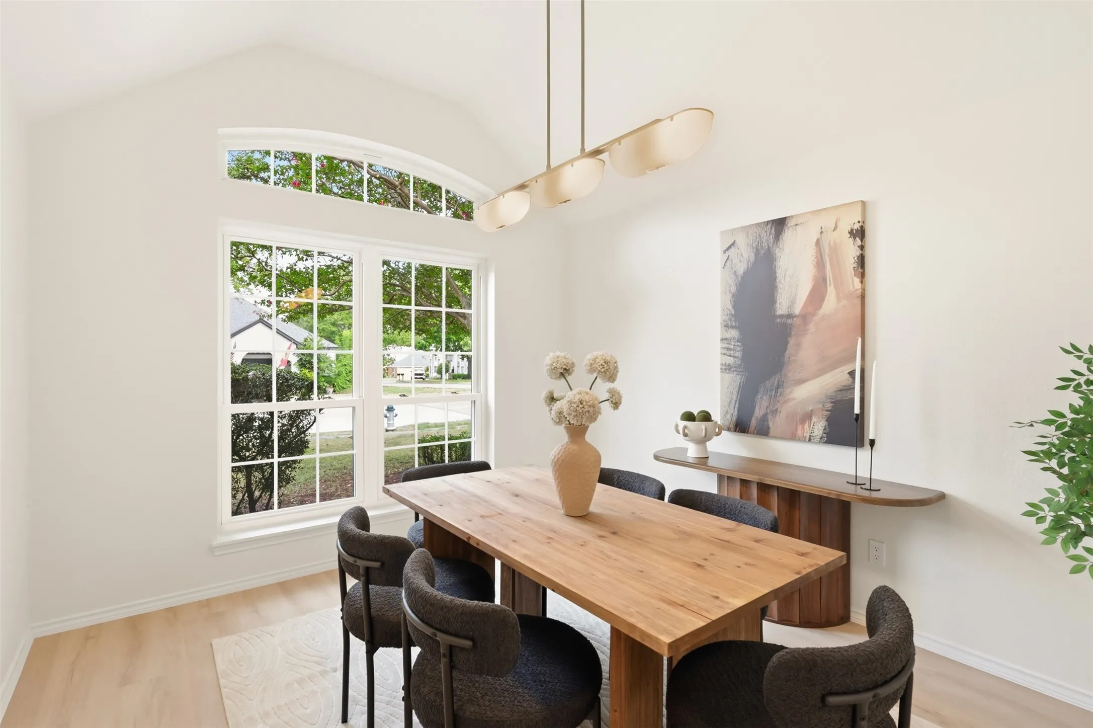 Vaulted ceiling, arched transom window, large grid-patterned window, wood-finish flooring, and a linear pendant light fixture