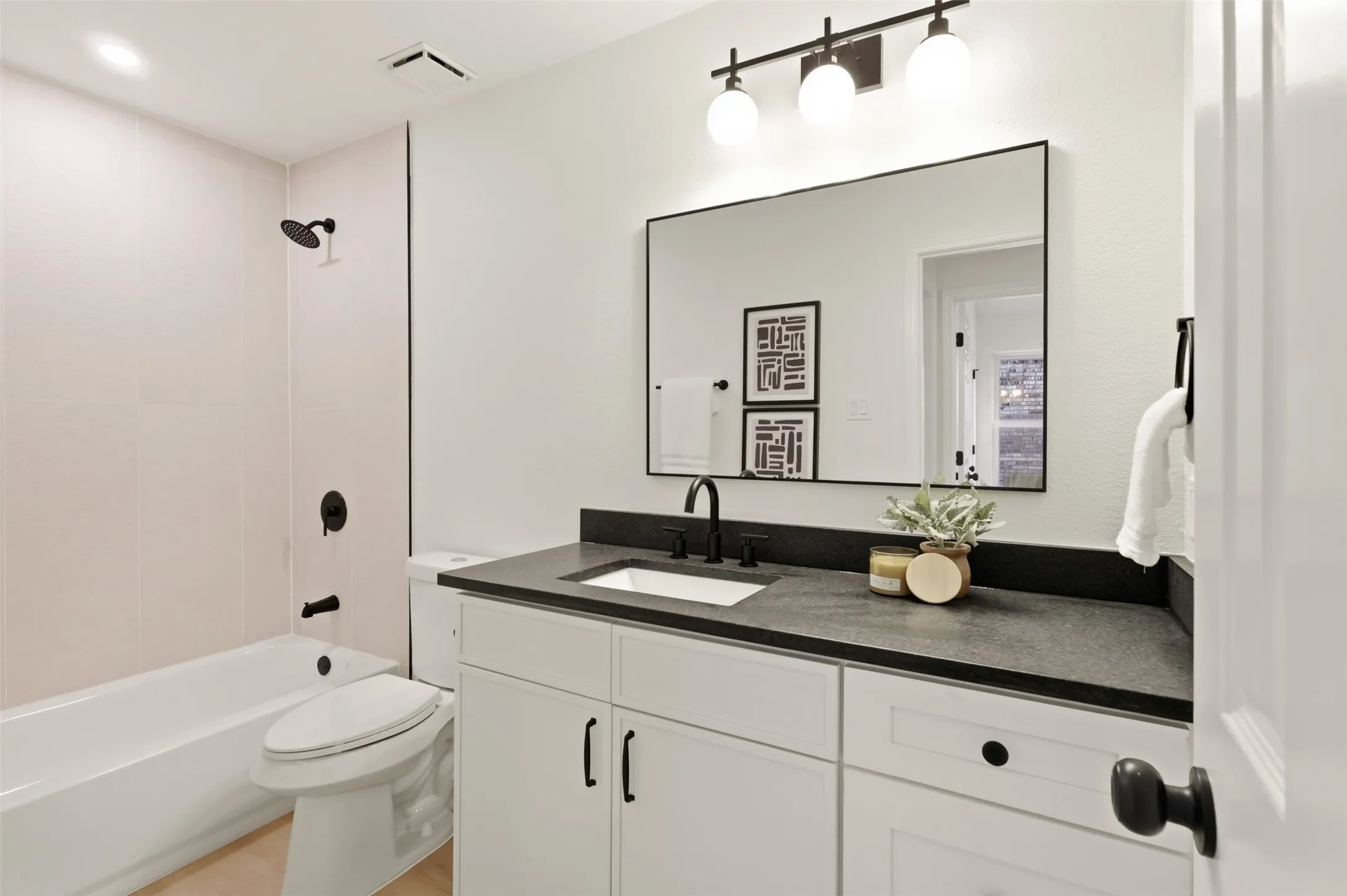 Bathroom featuring white cabinetry, a dark countertop, an undermount sink with a matte black faucet, and a large framed mirror