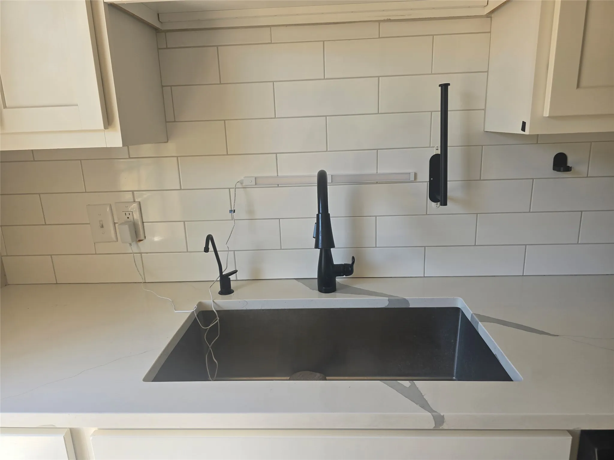 Undermount sink with a matte black faucet, light-toned countertop, and subway tile backsplash