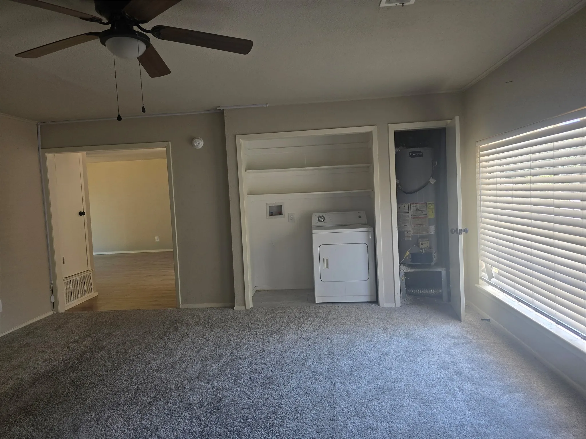 Carpeted room featuring a ceiling fan with light, a window with horizontal blinds, built-in shelving, and a laundry appliance hookup and converted garage into another living space.