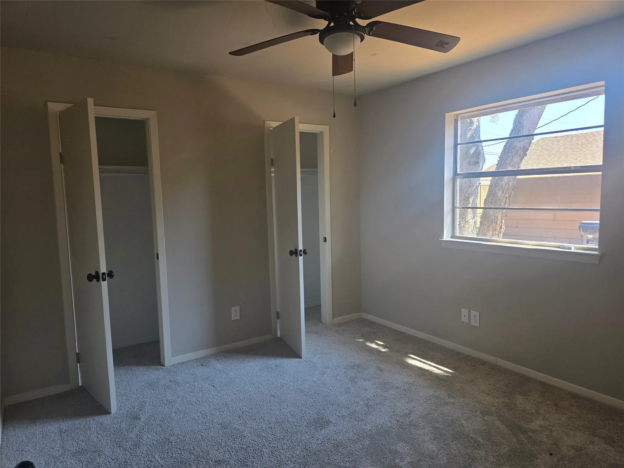 Carpeted room featuring a ceiling fan with integrated lighting, a window with horizontal muntins, and two closet spaces with bifold doors