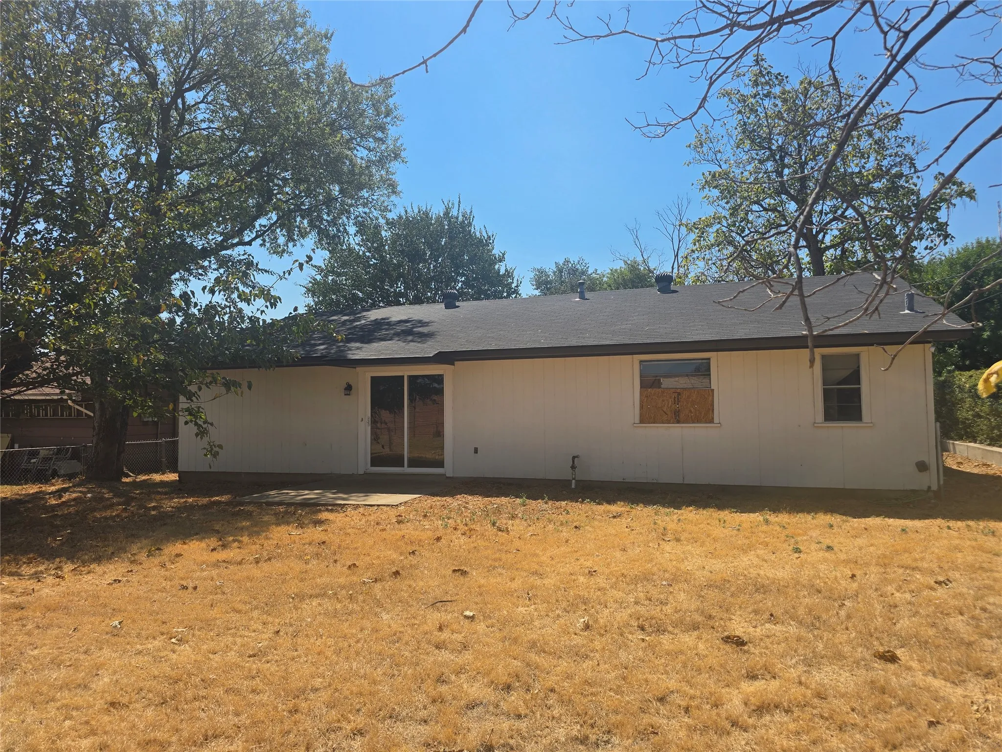 Expansive backyard featuring mature trees, a concrete patio, white siding, and a dark shingle roof
