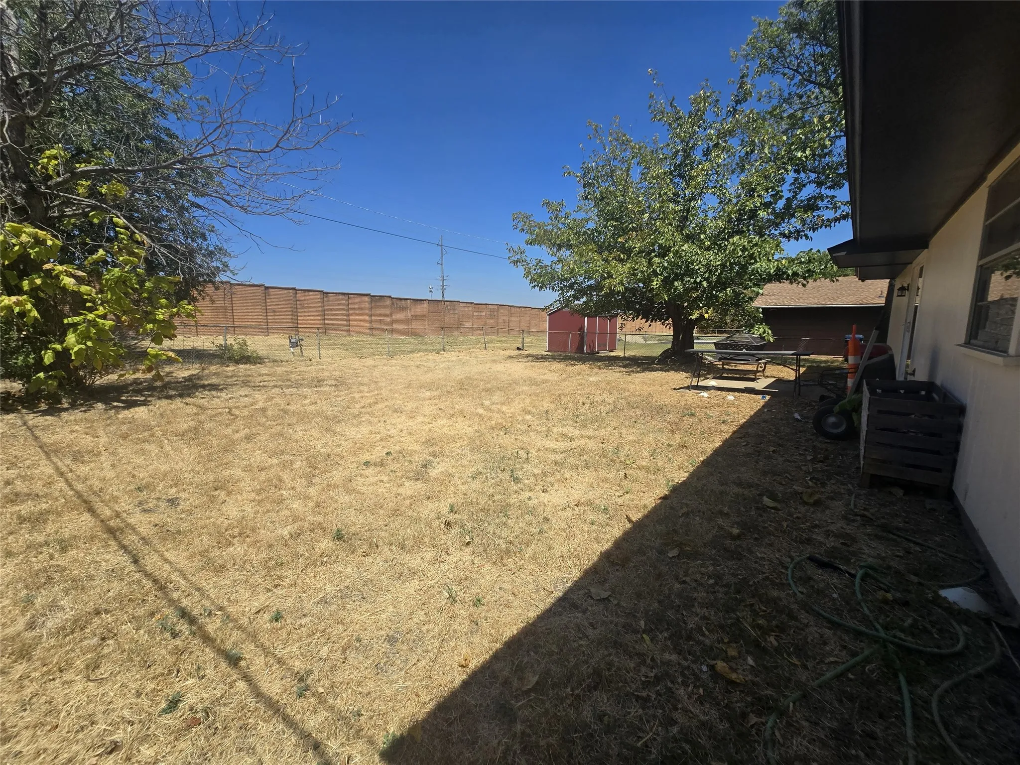 Expansive yard with mature trees, a privacy wall, and a detached storage shed