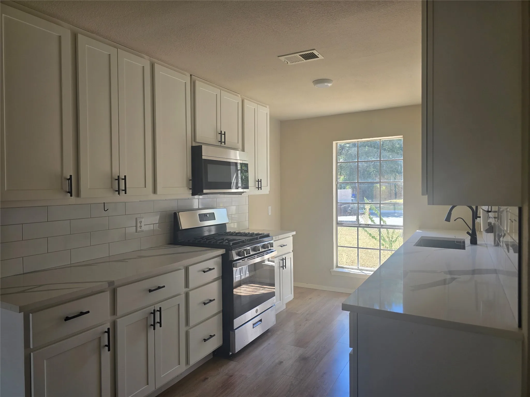 Kitchen featuring white shaker-style cabinetry, stainless steel appliances, a subway tile backsplash, and light wood-finish flooring