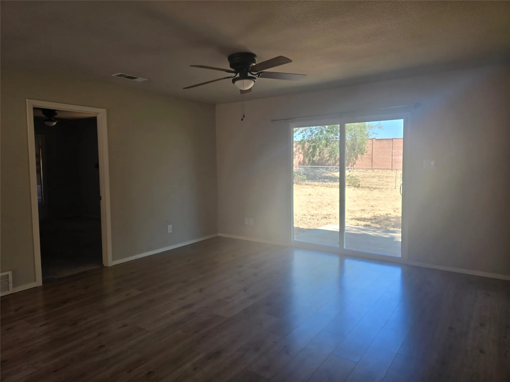 Wood-finish flooring, ceiling fan, neutral wall tones, sliding glass door, and a spacious outdoor area