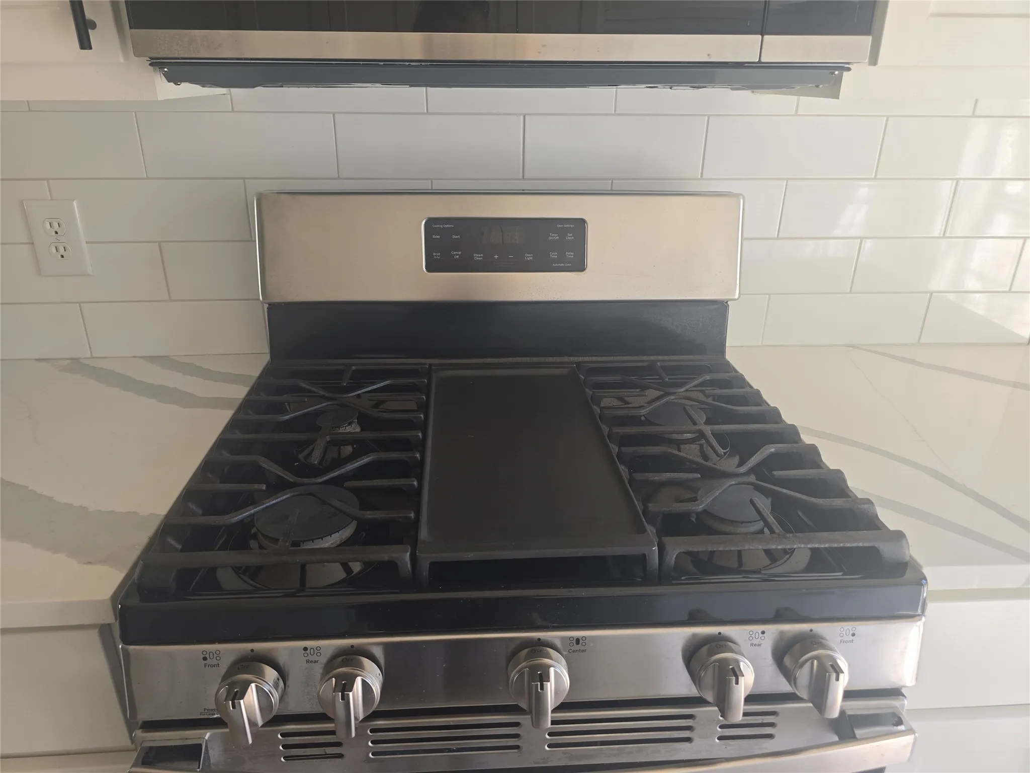 Stainless steel gas range with a griddle, subway tile backsplash, and light-toned countertop