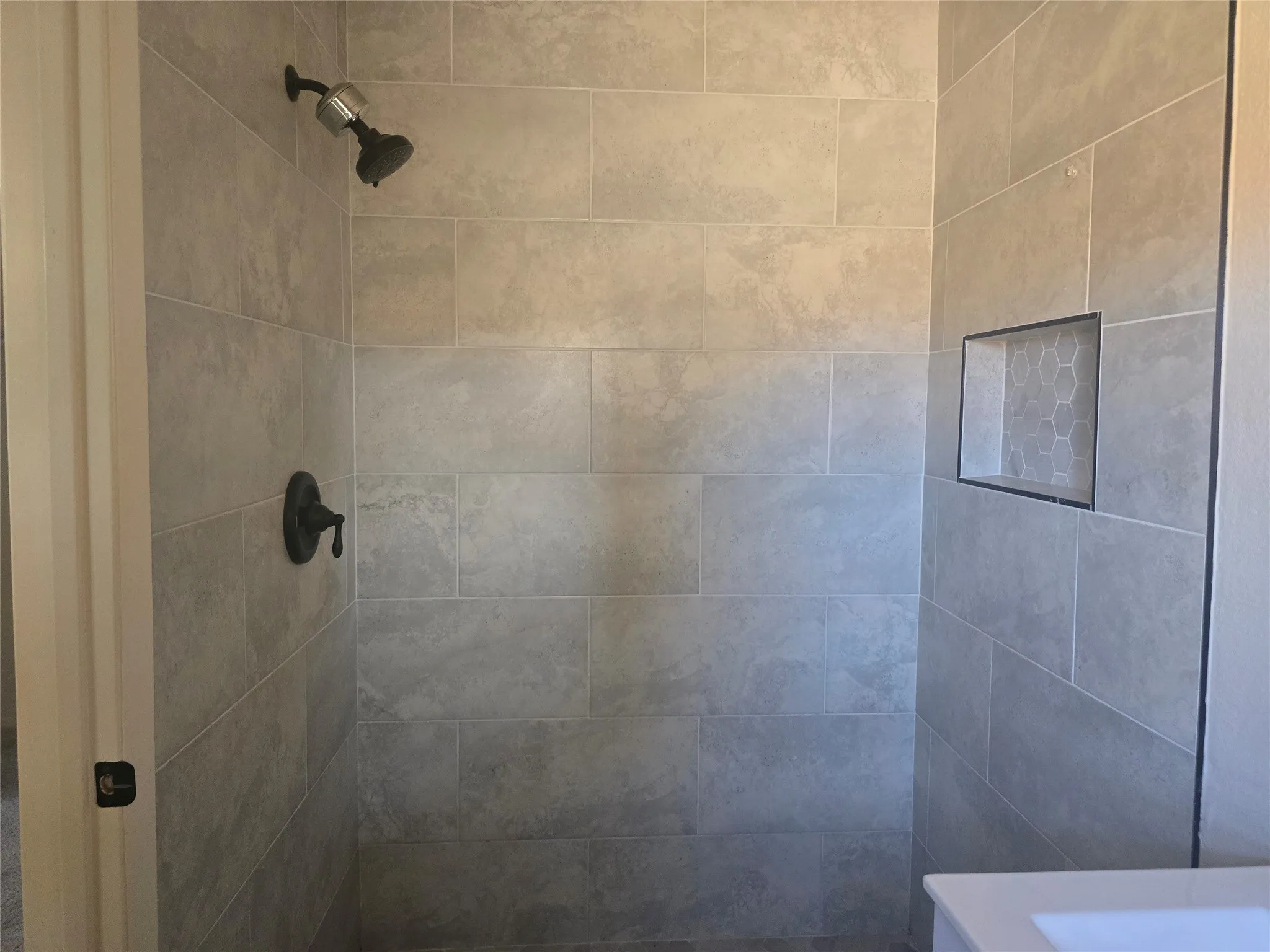 Tiled shower with a built-in niche featuring hexagonal mosaic tile, oil-rubbed bronze shower fixtures, and a white vanity with an integrated sink