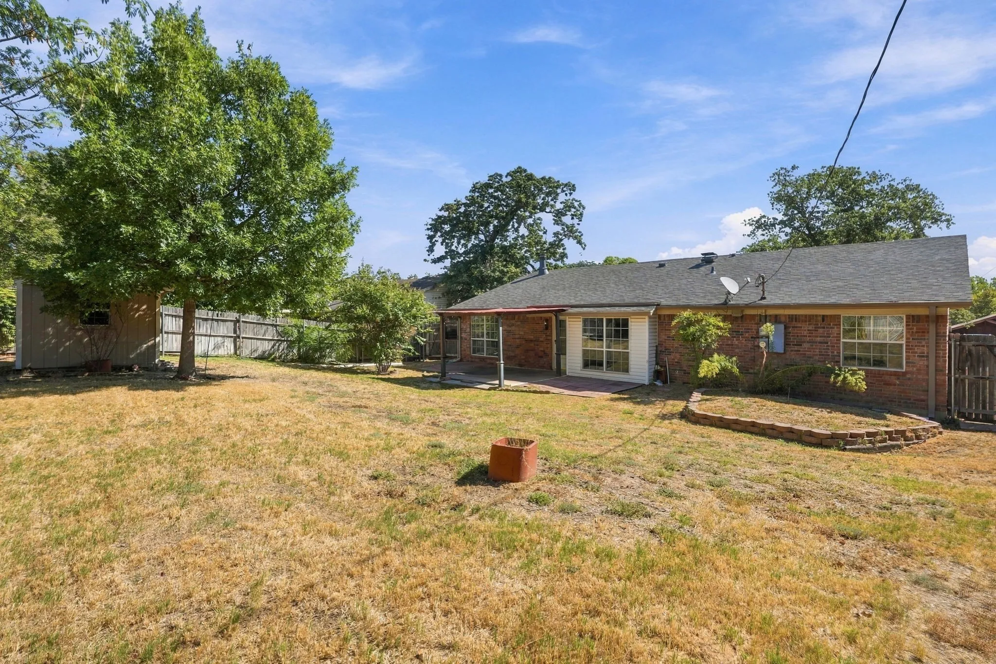 Expansive backyard with a storage shed, mature tree, brick retaining wall, and covered patio