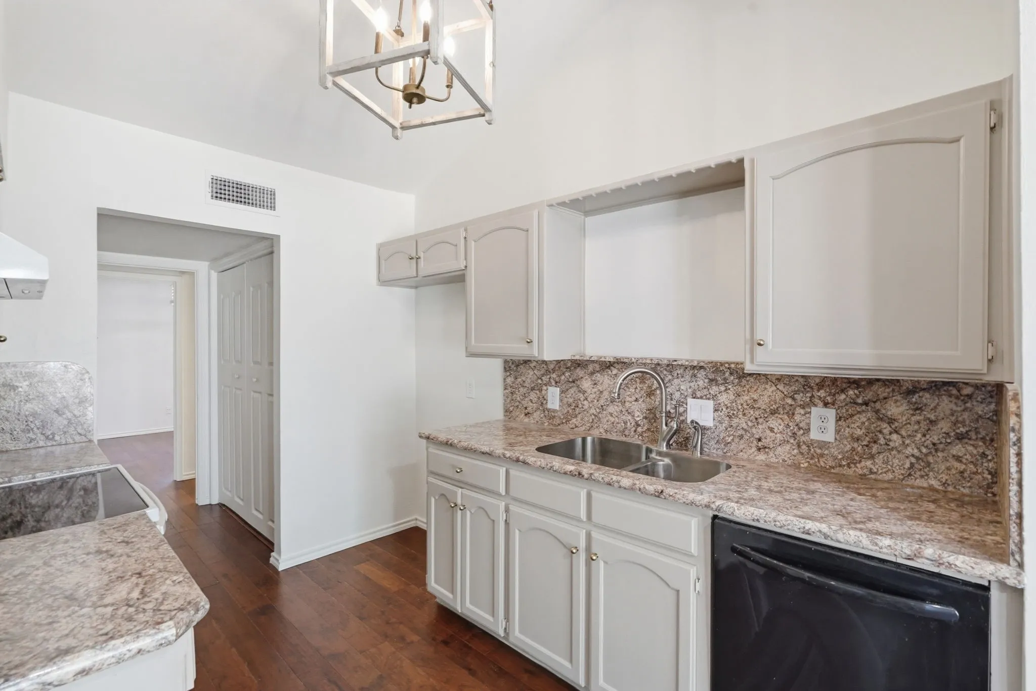 Kitchen featuring wood-finish flooring, light-toned cabinetry, granite-style countertops, stainless steel double basin sink, and a black dishwasher