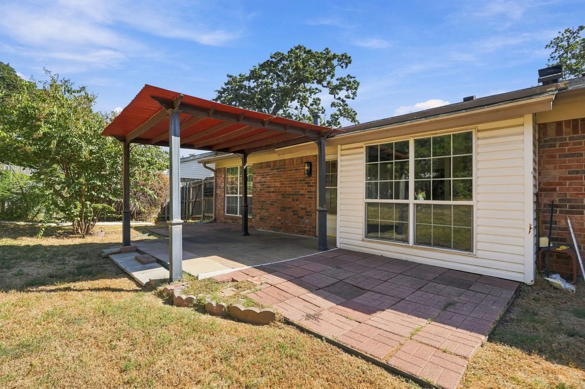Red-roofed covered patio with concrete and brick paver flooring, set against a brick and siding exterior
