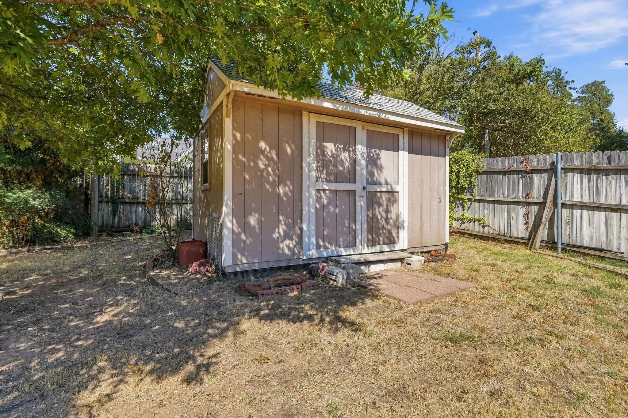Wooden storage shed with double doors, wood-paneled siding, and an asphalt shingle roof