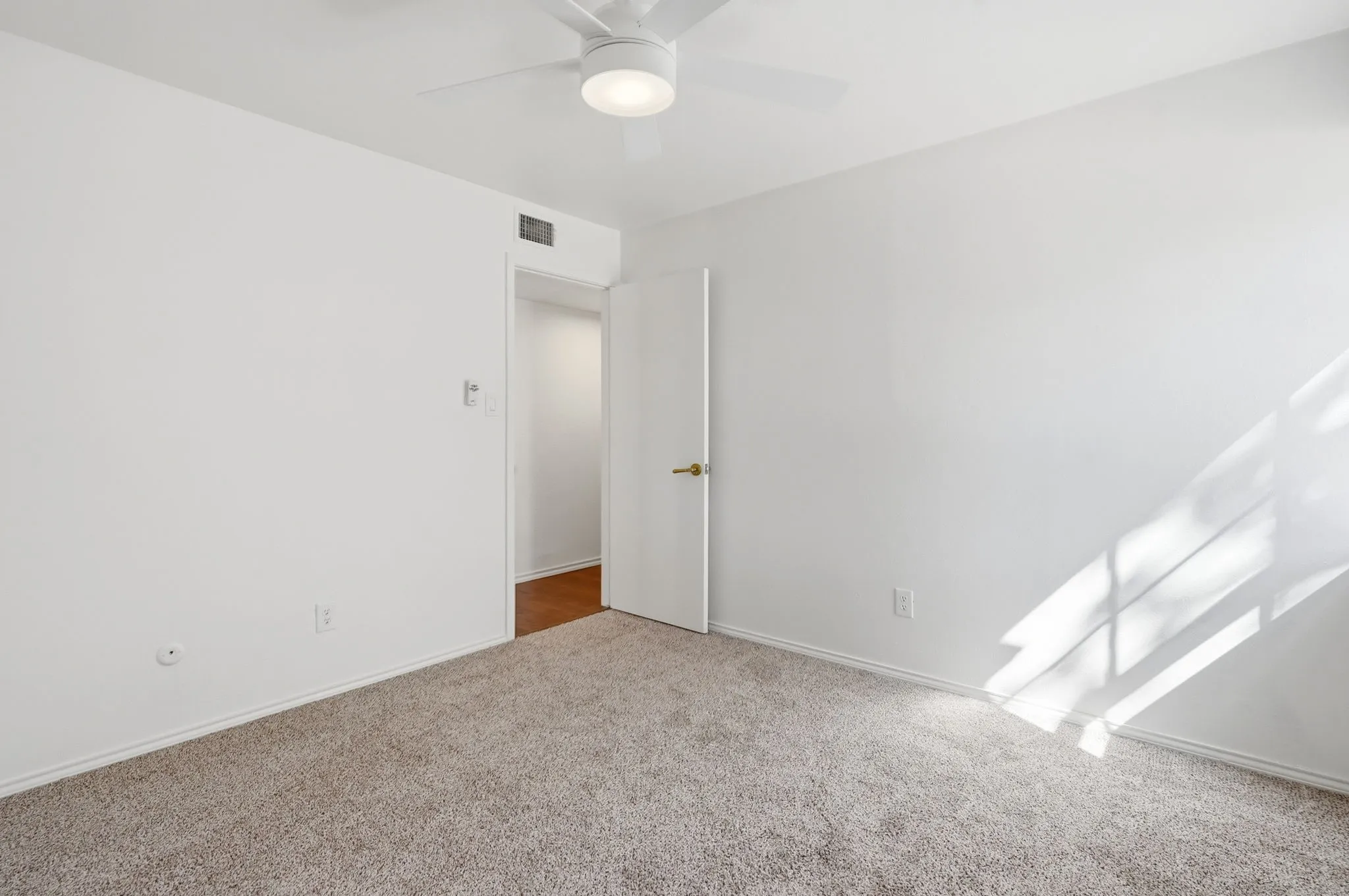 Plush carpeting throughout, white painted walls, and a ceiling fan with integrated lighting