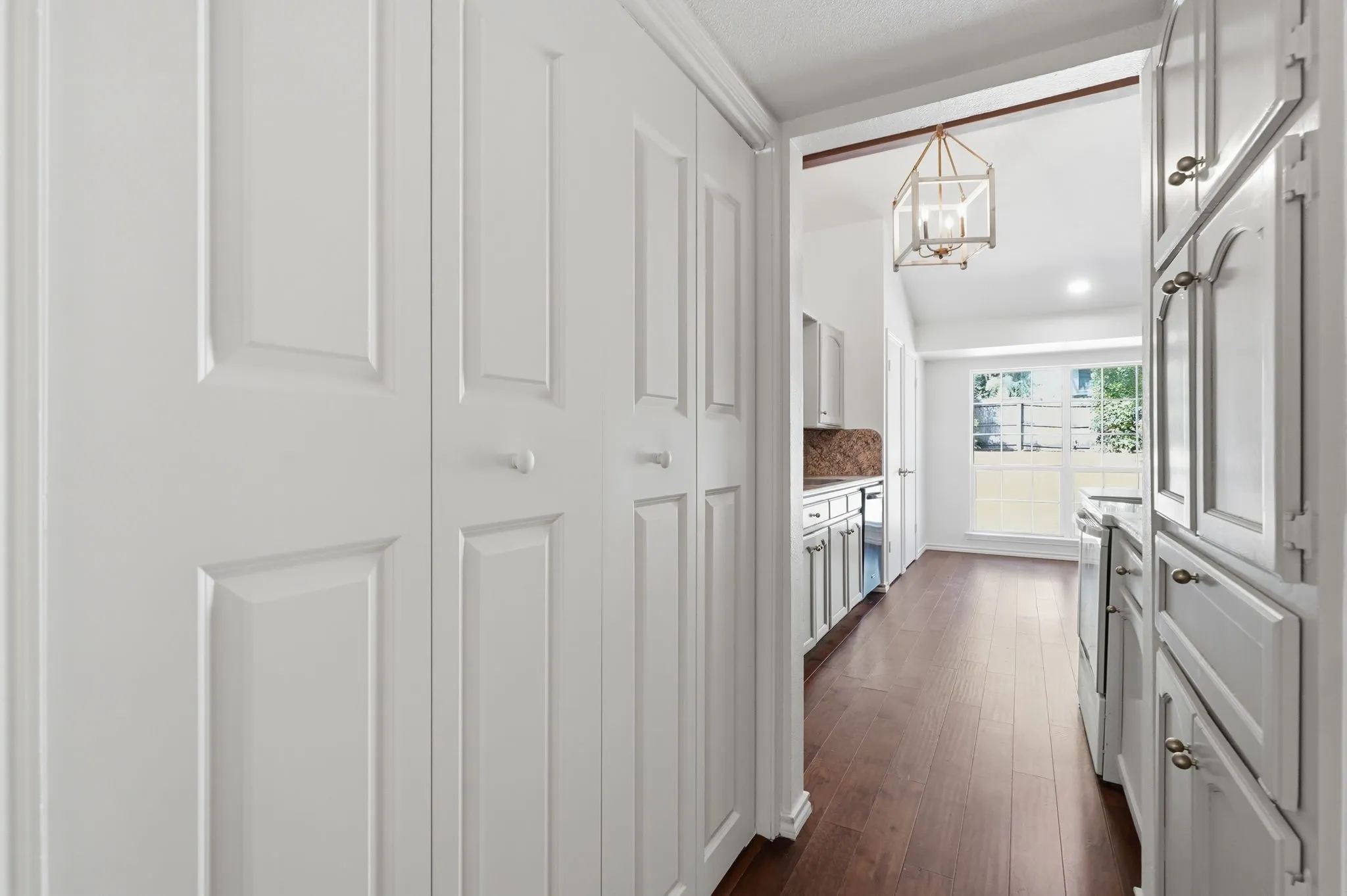 White paneled bifold closet doors, wood-finish flooring, white cabinetry with decorative hardware, and a ceiling-mounted lantern light fixture