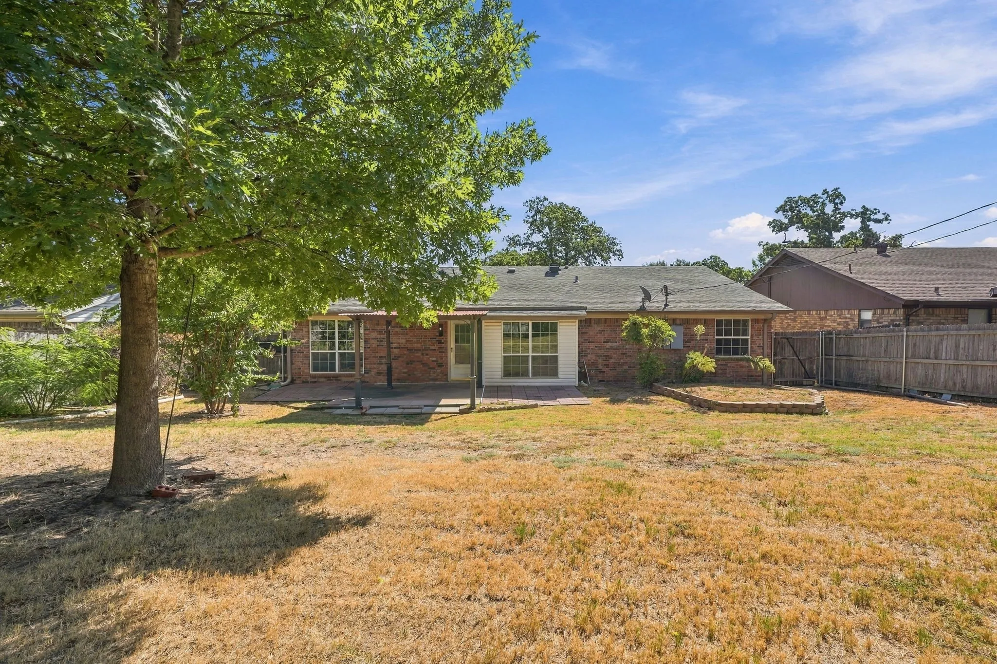 Backyard featuring a brick exterior, multiple windows, a rear patio, and a privacy fence