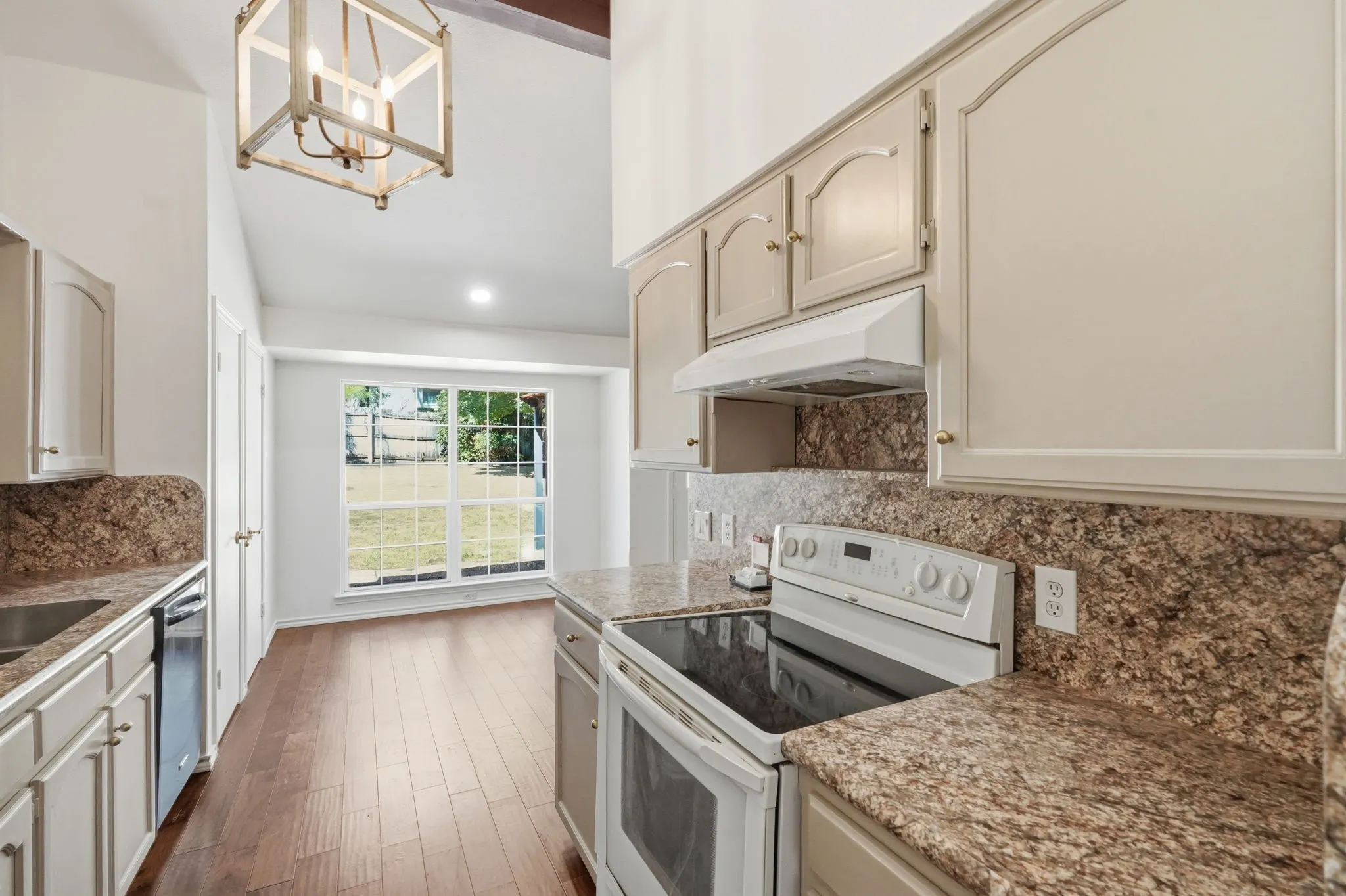 Kitchen featuring wood-finish flooring, vaulted ceilings, pendant light fixture, built-in cabinetry, and stone countertops