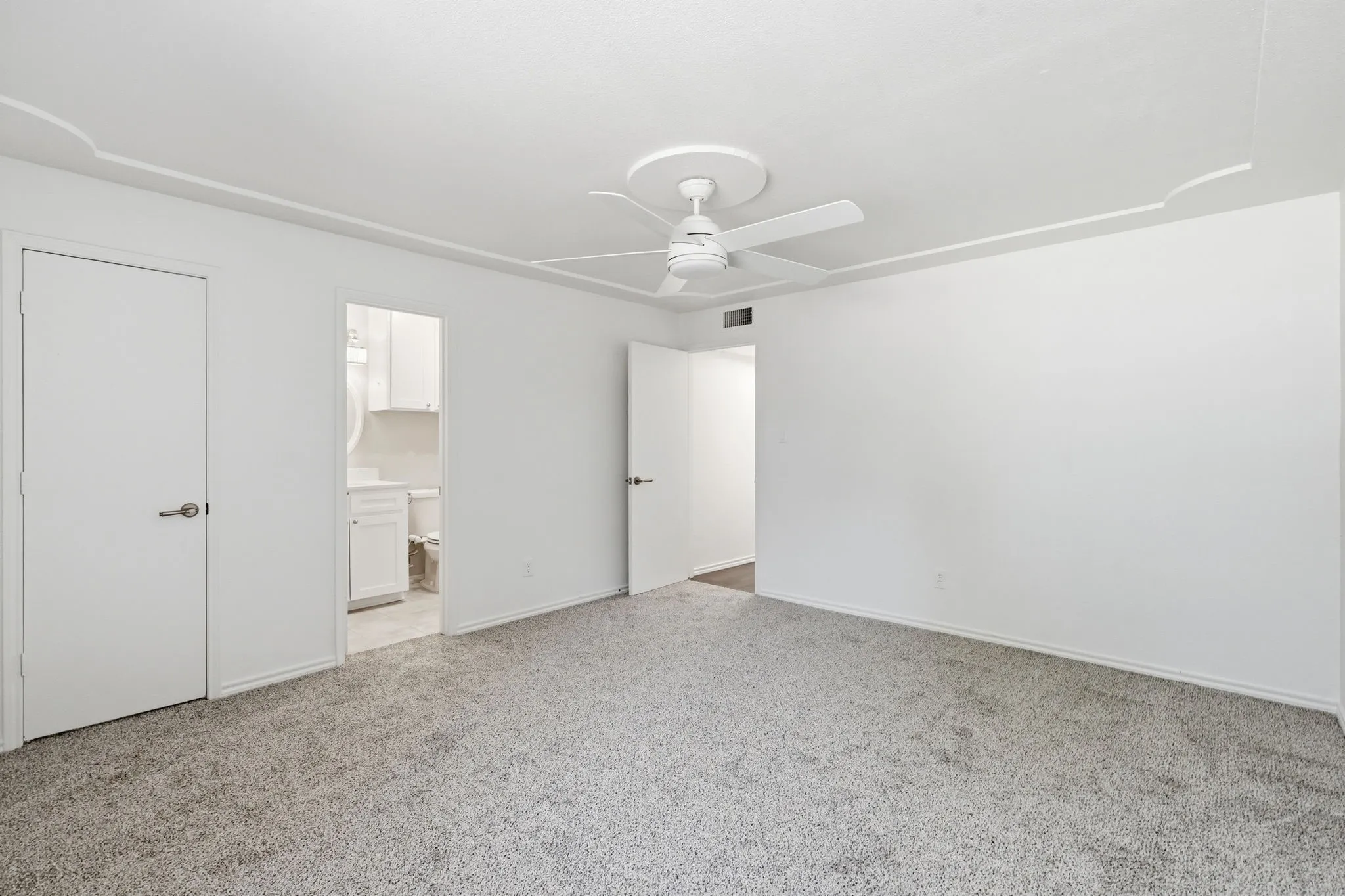 Plush grey carpeting, white ceiling fan, recessed ceiling detail, and solid white doors with brushed nickel hardware