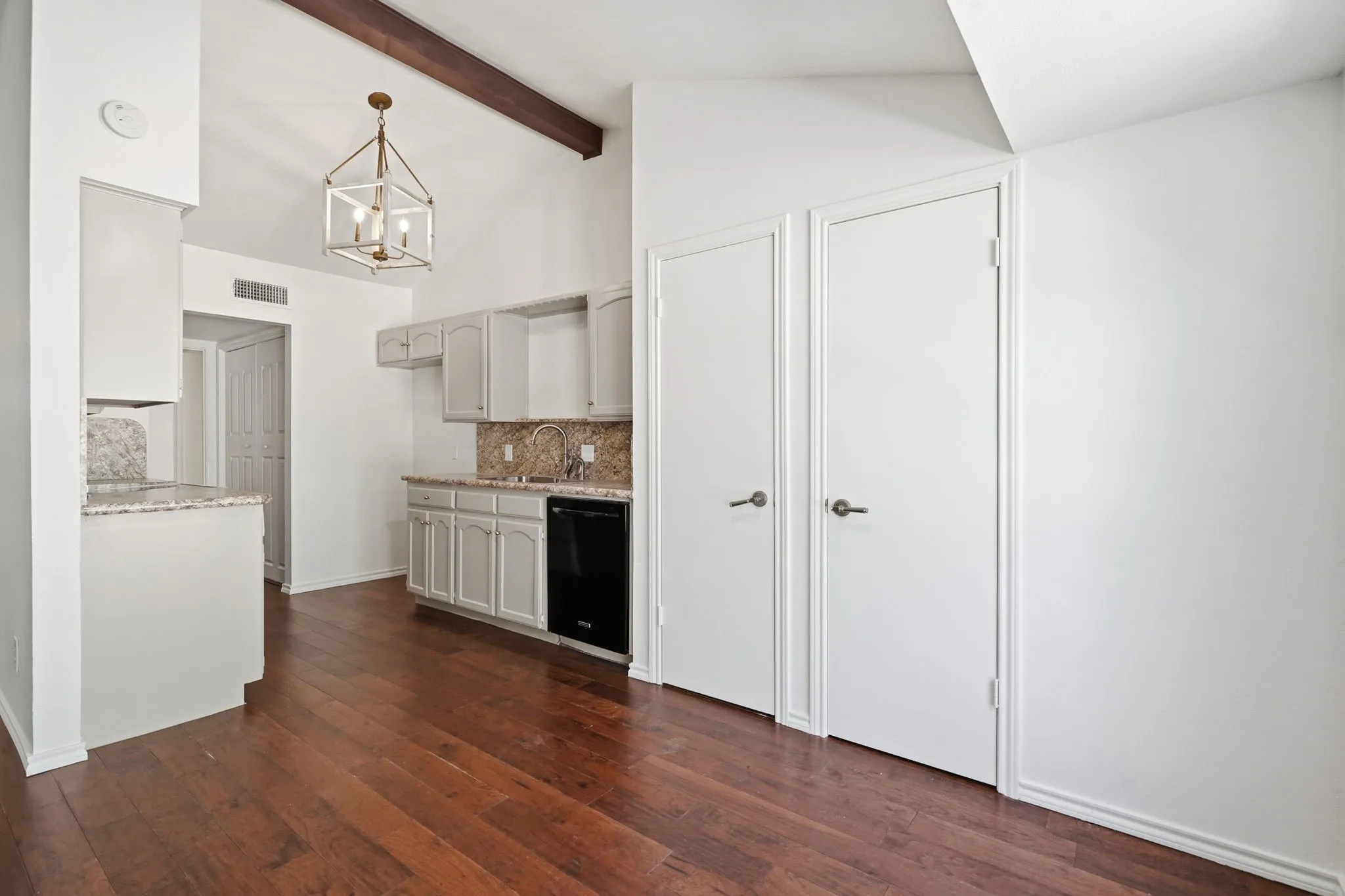 Vaulted ceiling with an exposed wood beam, wood-finish flooring, painted cabinetry, and stone countertops