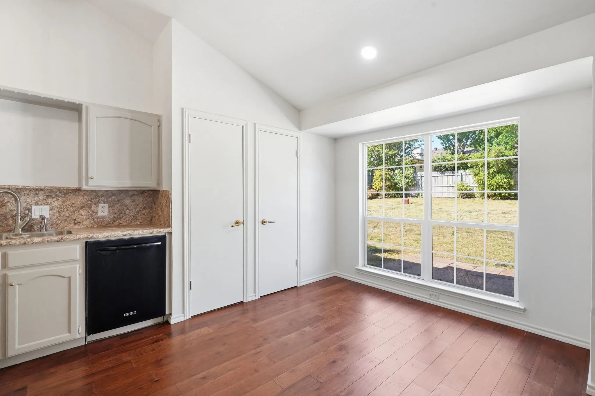 Varnished wood-finish flooring, vaulted ceiling, built-in cabinetry, granite-style countertops, and a large multi-pane window